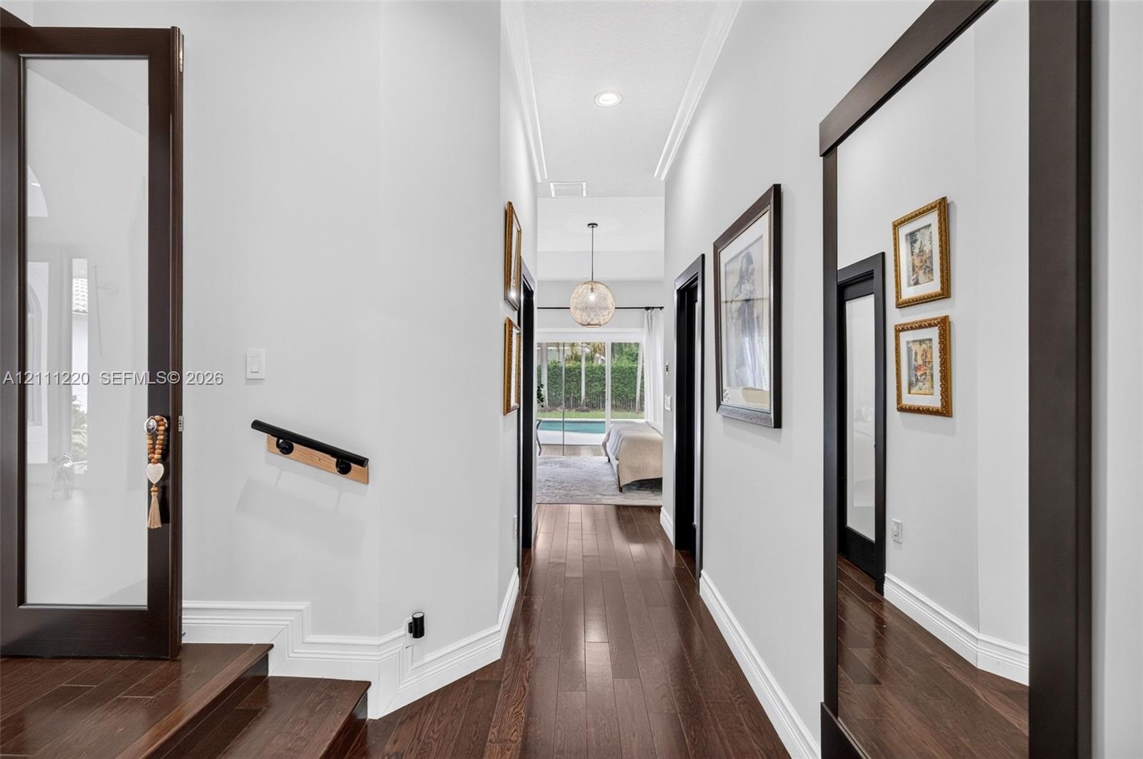 Hallway featuring dark wood-finish flooring, high ceilings with recessed lighting, crown molding, a decorative globe pendant fixture, and glass-panele