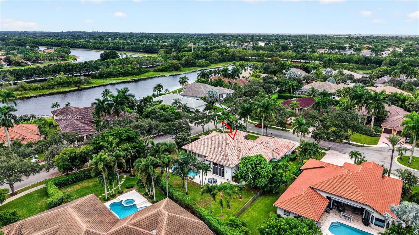 Aerial perspective of a single-story residence featuring a tile roof, light-toned exterior finish, and a private rear swimming pool, situated in a lan