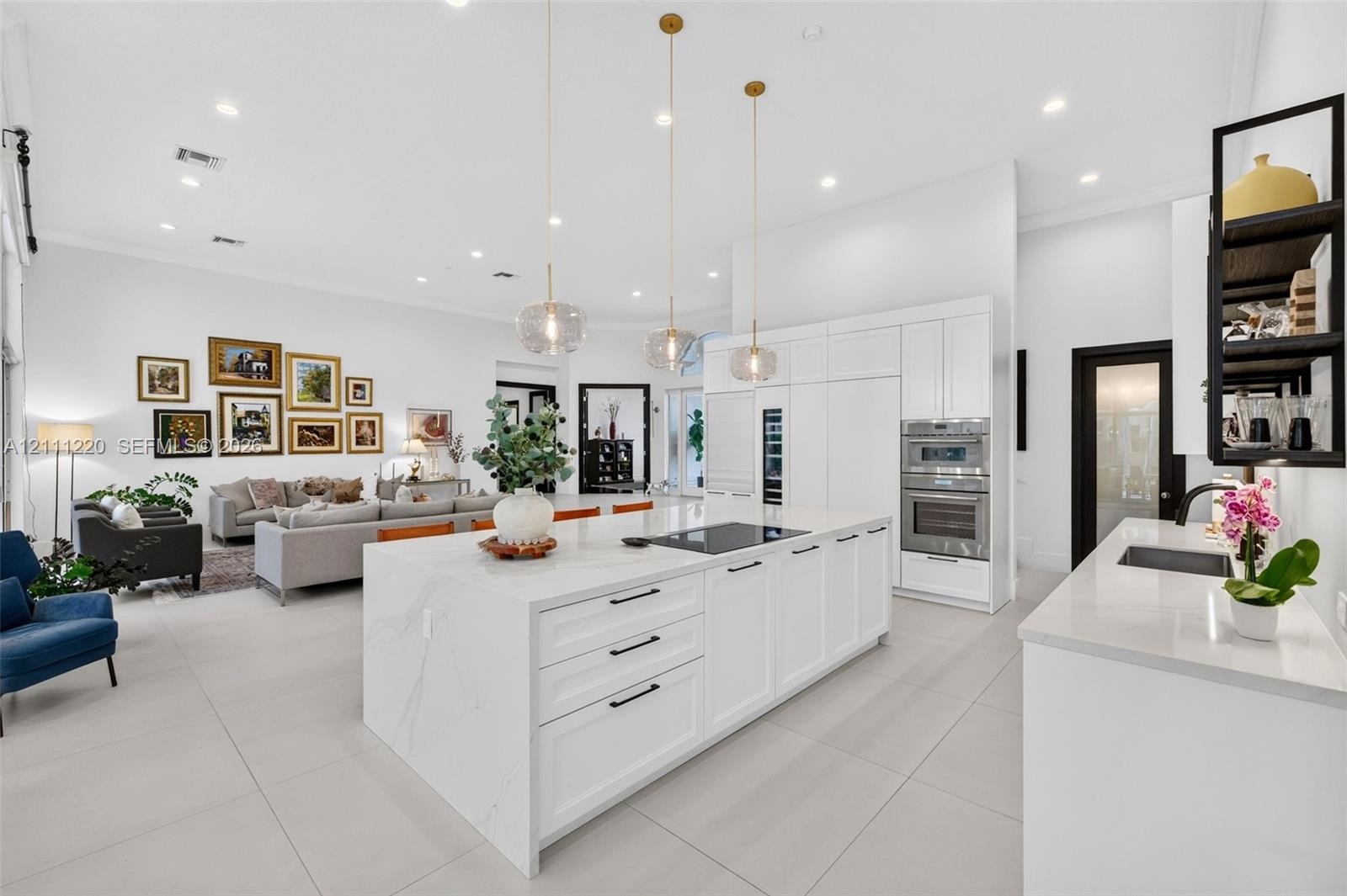 Kitchen featuring a large central island with quartz surfacing, white shaker-style cabinetry, stainless steel double wall ovens, three glass pendant l