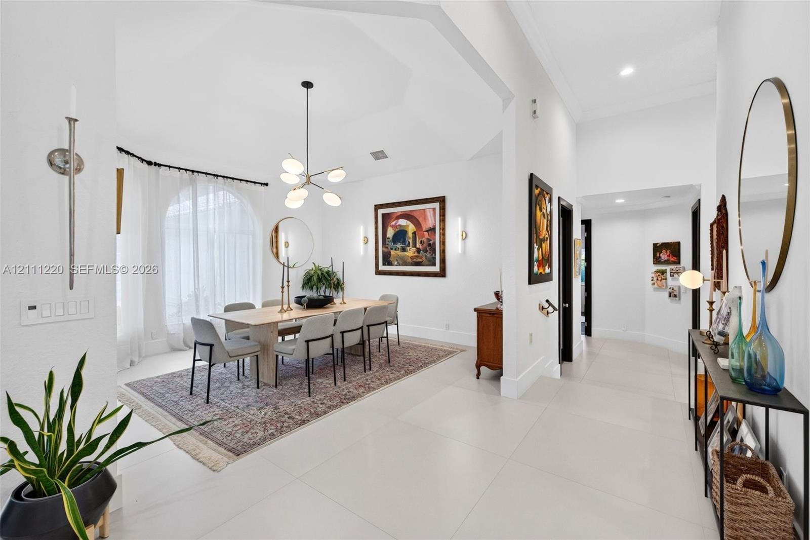 Dining area featuring a vaulted ceiling, arched window, oversized tile flooring, and a multi-arm chandelier