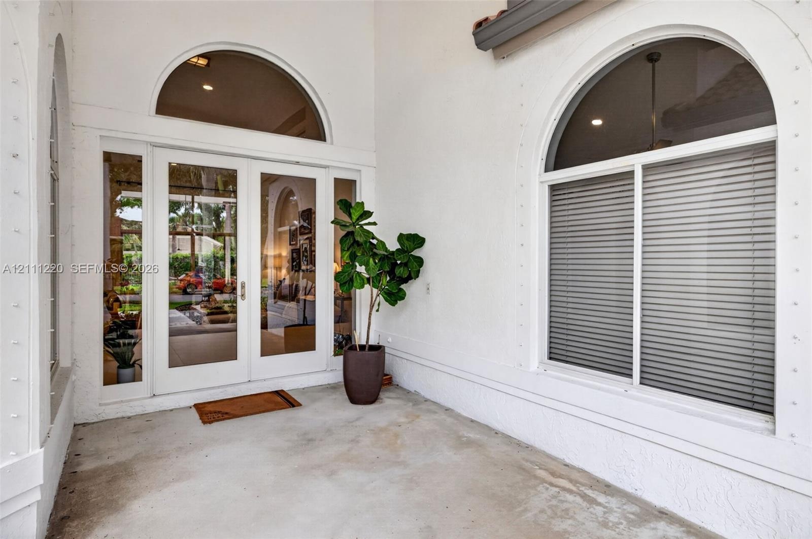 Covered entryway featuring double-glass doors, arched transom windows, and white stucco exterior finish