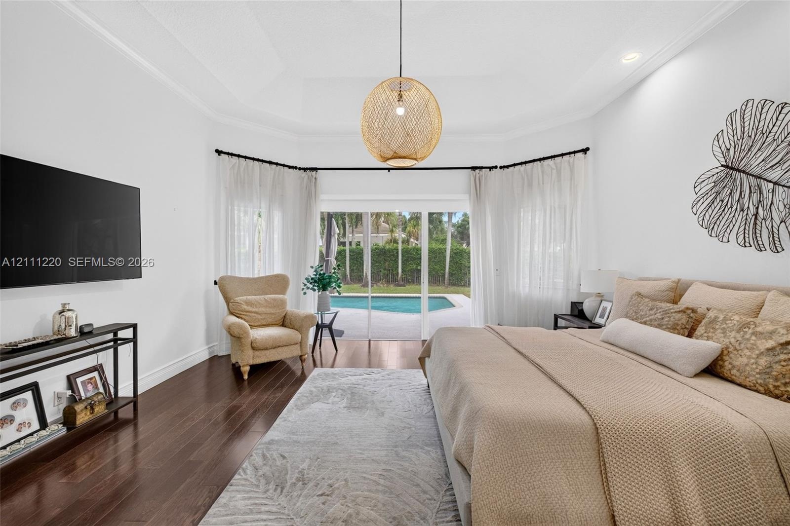 Tray ceiling, wood-finish flooring, and glass sliding doors providing exterior exposure to a swimming pool