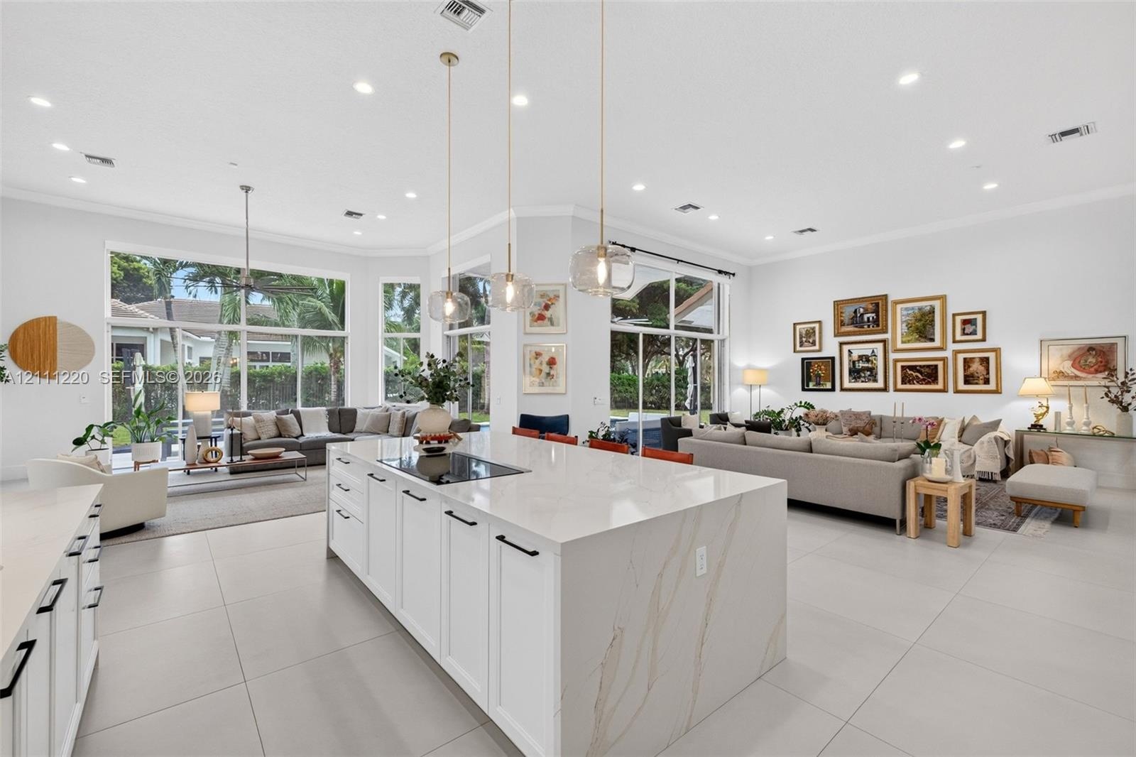 Large kitchen island with a stone-finish waterfall countertop, integrated cooktop, white shaker-style cabinetry, matte black hardware, and three glass