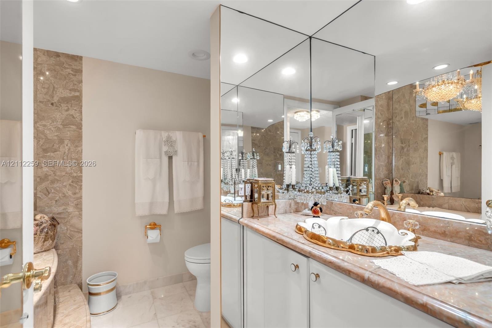 Vanity featuring a custom-shaped basin with gold-tone trim, integrated stone countertop, floor-to-ceiling mirror, and wall-mounted crystal chandelier-