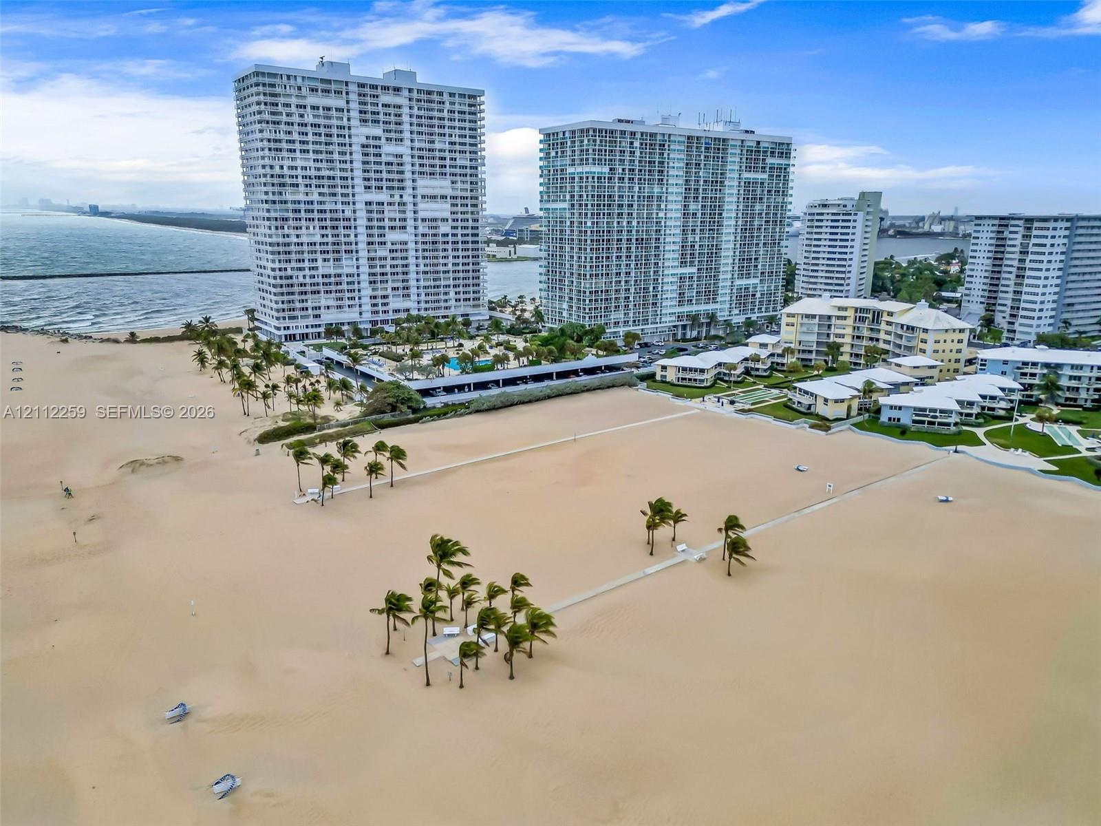 Direct oceanfront location featuring a sprawling sandy beach, clusters of mature palm trees, and elevated multi-story residential towers