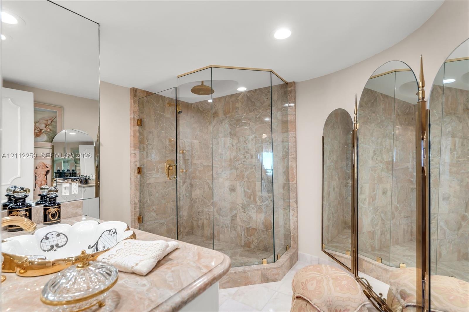 Walk-in corner shower with glass enclosure and stone-tiled surround, stone-topped vanity, and arched wall-mounted mirrors