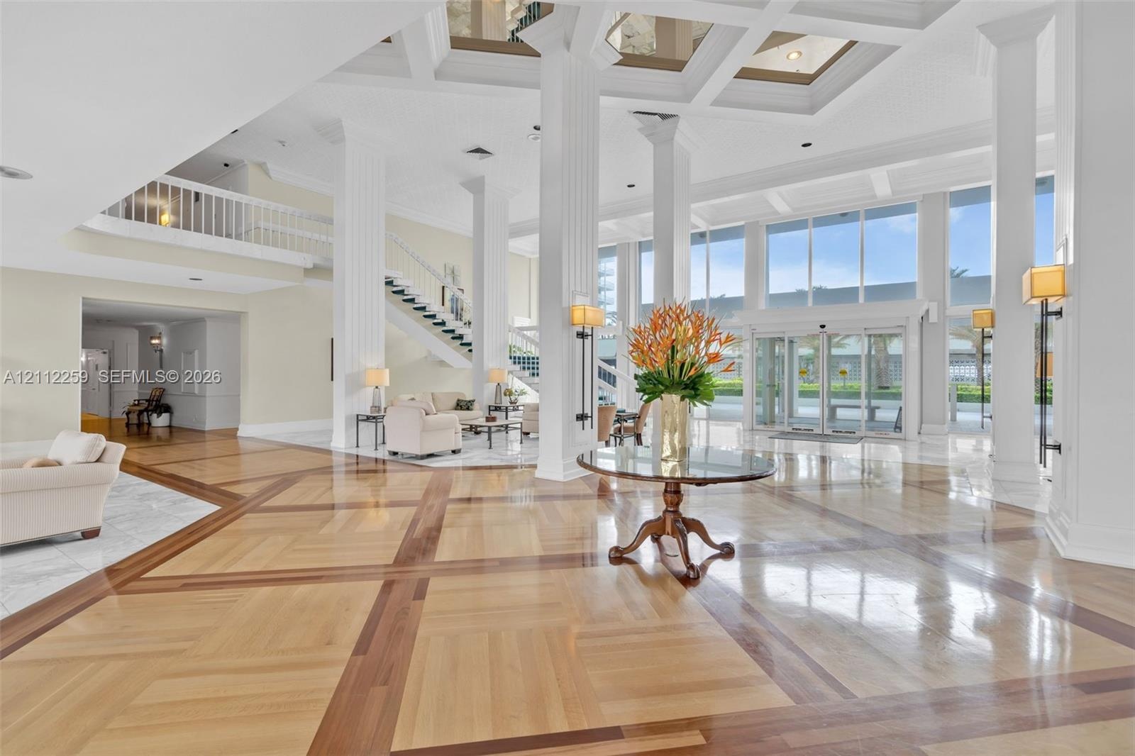 Grand atrium featuring a coffered ceiling, polished wood-finish flooring with intricate inlay, soaring structural columns, expansive floor-to-ceiling 