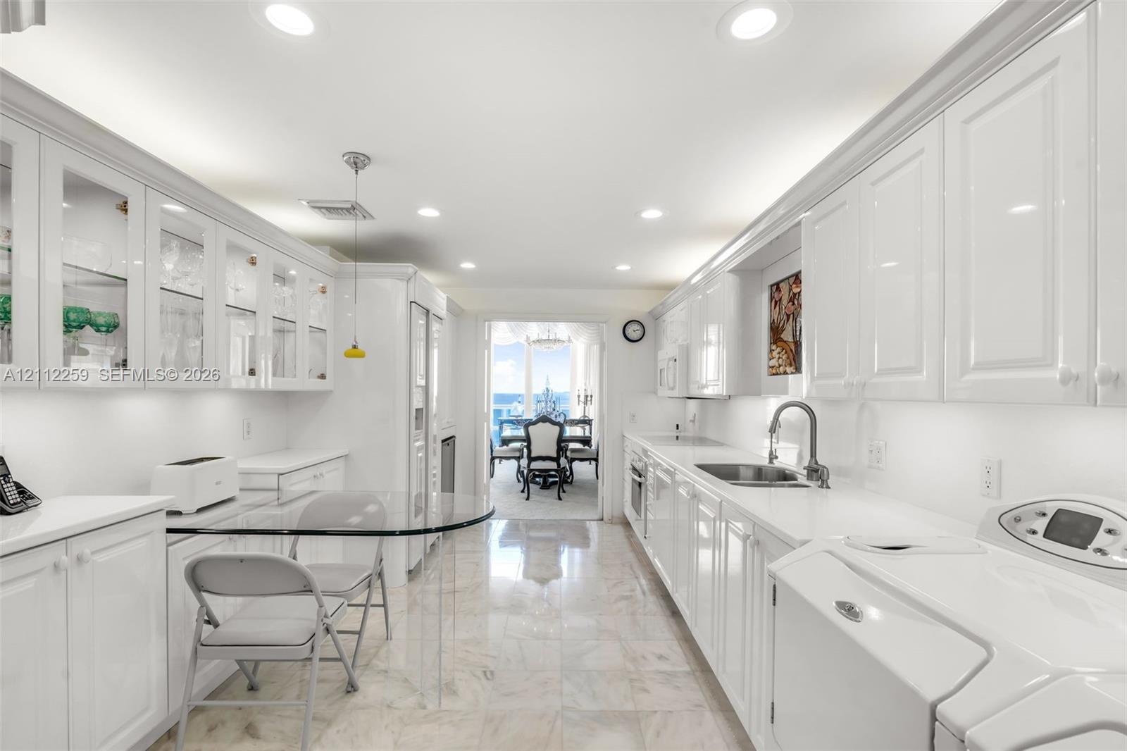 Galley-style kitchen featuring high-gloss white cabinetry, glass-front upper displays, stone-finish flooring, recessed lighting, and a single-basin un