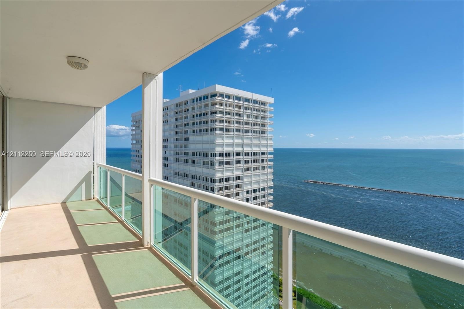 Covered balcony featuring glass pane railings, solid support columns, and water horizon exposure