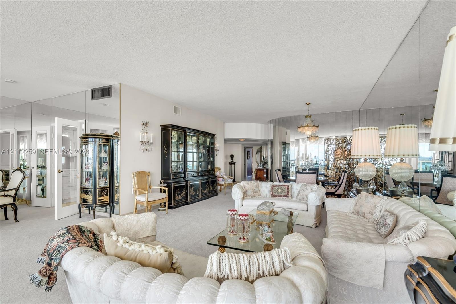 Expansive living space featuring wall-to-wall mirrored surfaces, a built-in floor-to-ceiling cabinet, dual multi-tiered chandeliers, and neutral wall-