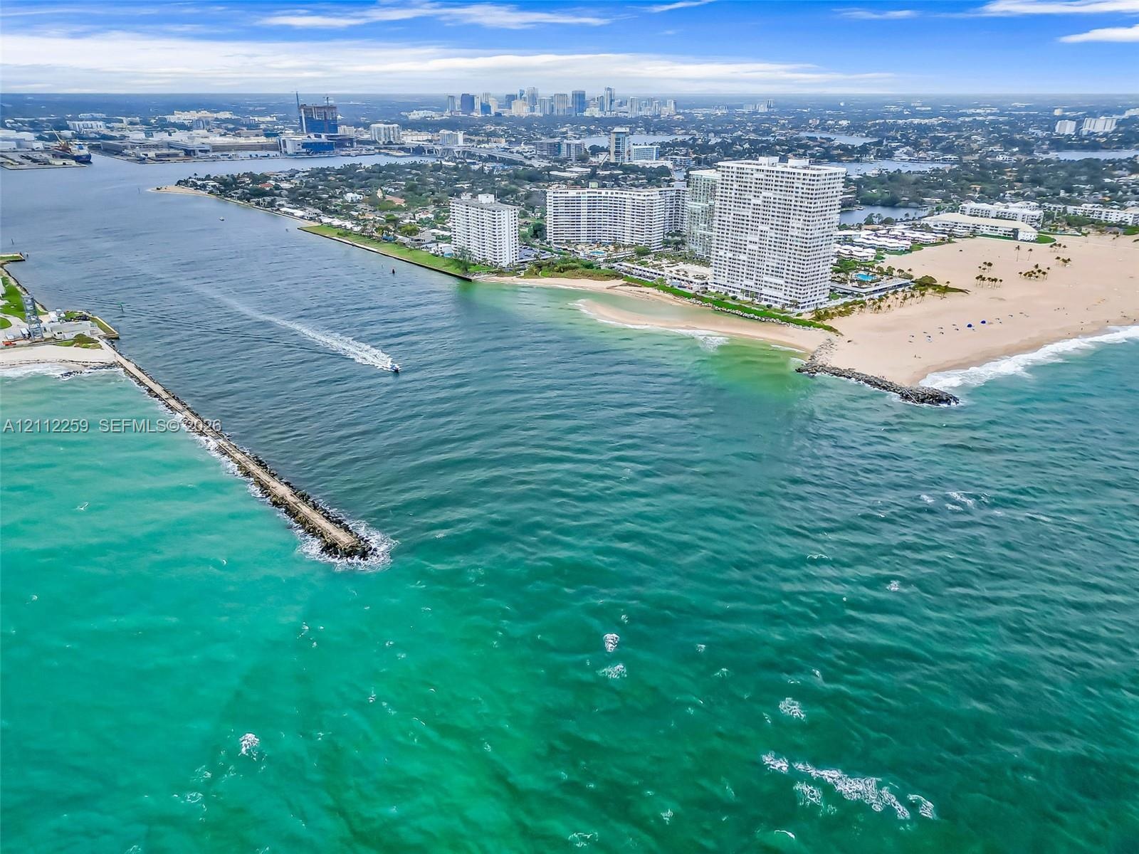 Aerial perspective of the coastline featuring expansive ocean frontage, stone jetties, sandy beaches, and high-rise structures