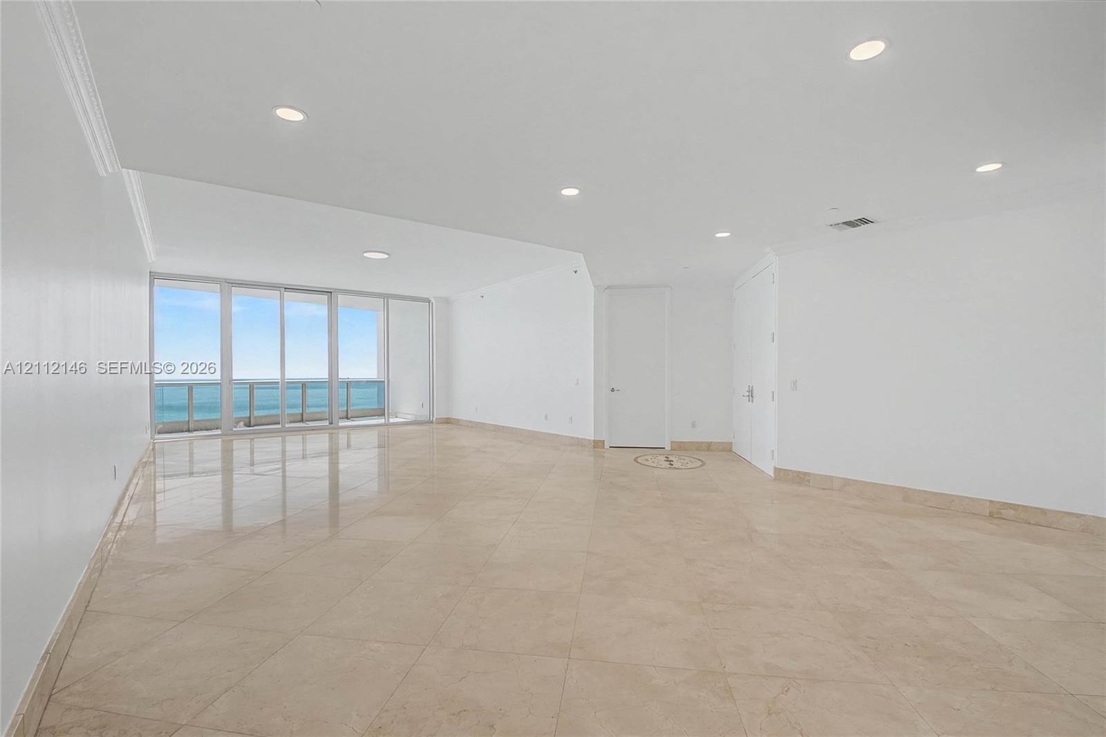 Open-concept interior featuring large-format tile flooring, recessed lighting, floor-to-ceiling glass sliding doors, and a balcony with coastal scener