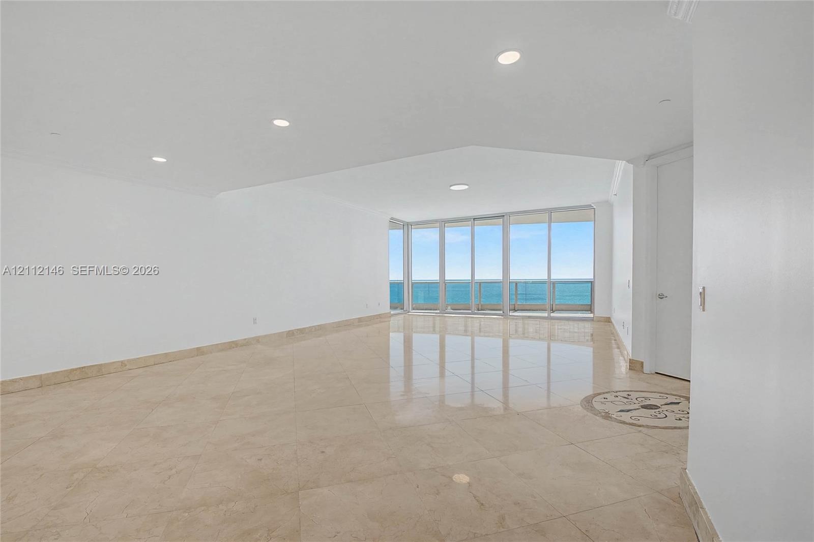 Expansive interior space featuring large-format tile flooring, recessed lighting, and floor-to-ceiling glass paneling with an exterior balcony