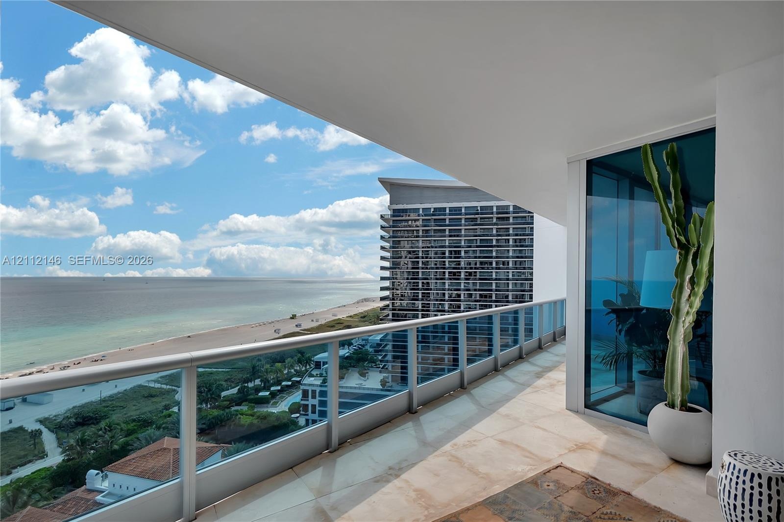 Covered balcony featuring stone tile flooring and glass pane railing with metal accents