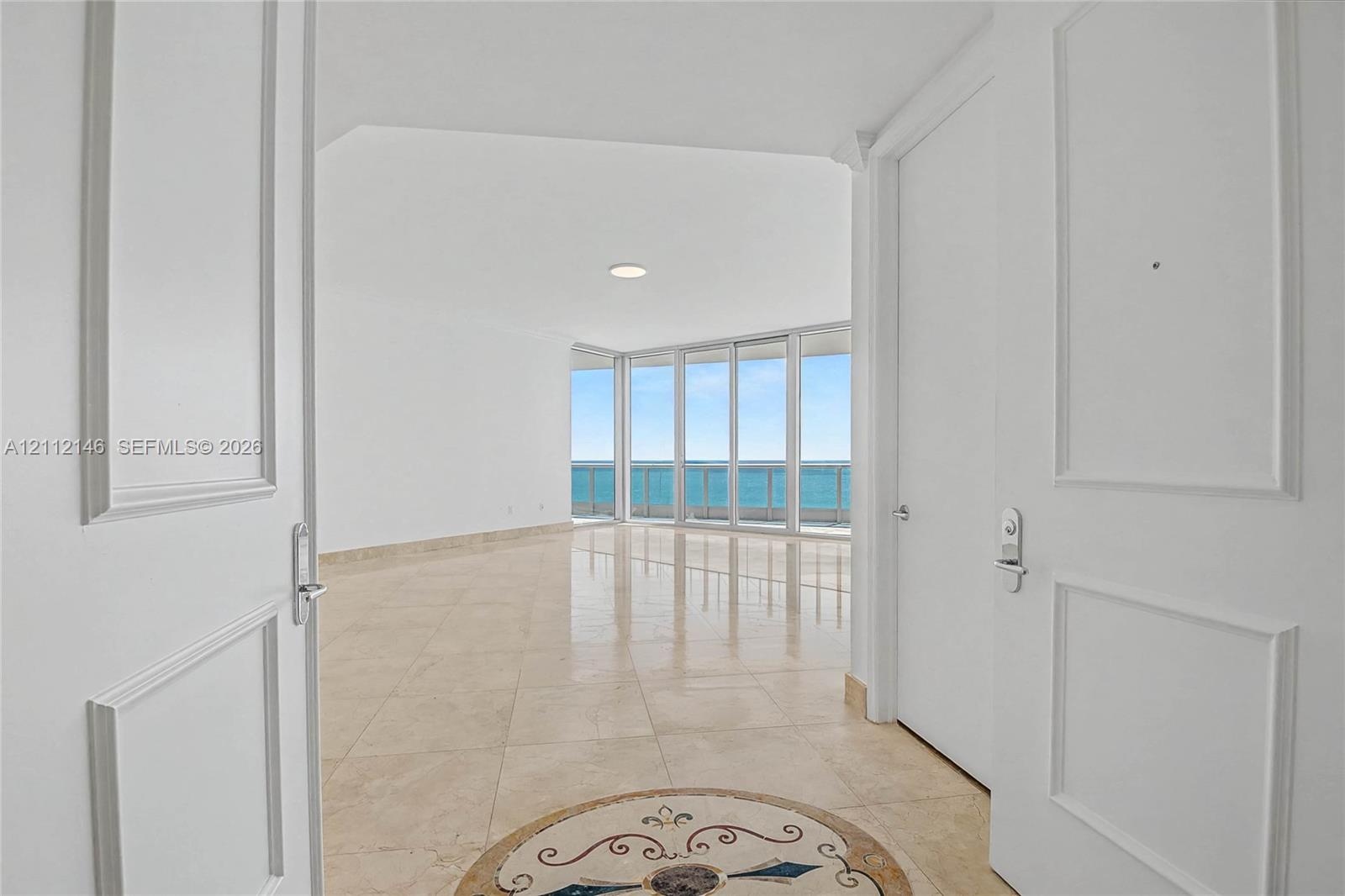 Interior entry featuring dual-panel doors, large-format tile flooring with a circular stone inlay medallion, and floor-to-ceiling glass windows offeri