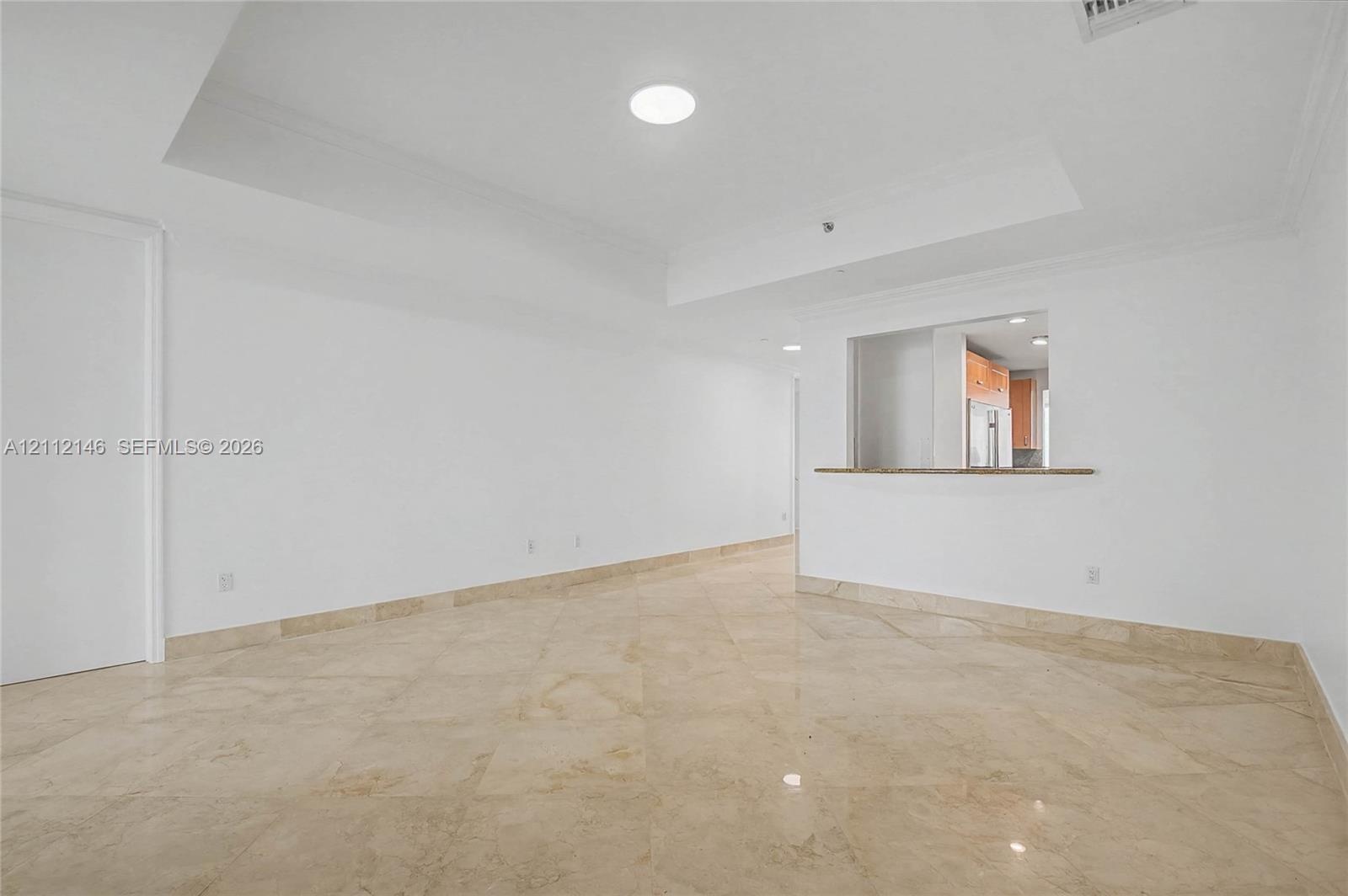 Open-concept interior featuring high tray ceilings, polished natural stone flooring, and a pass-through counter with a stone surface