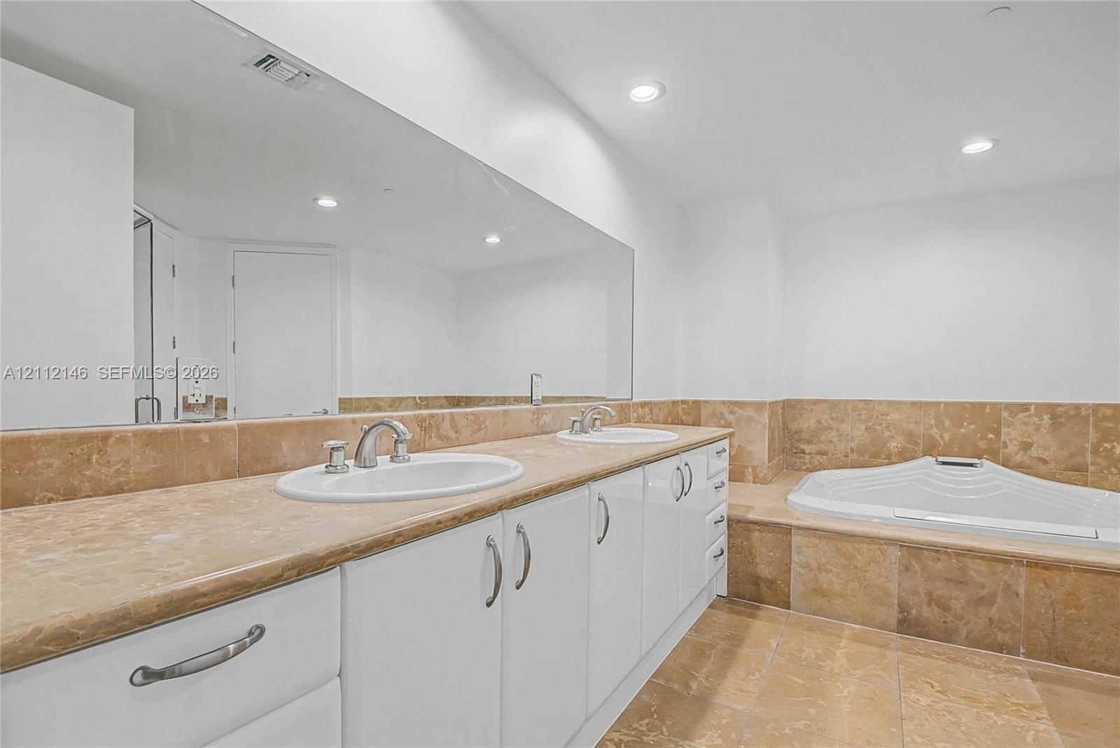 Bathroom featuring a dual-sink vanity with stone countertops, a large wall-to-wall mirror, recessed lighting, and a stone-tiled soaking tub