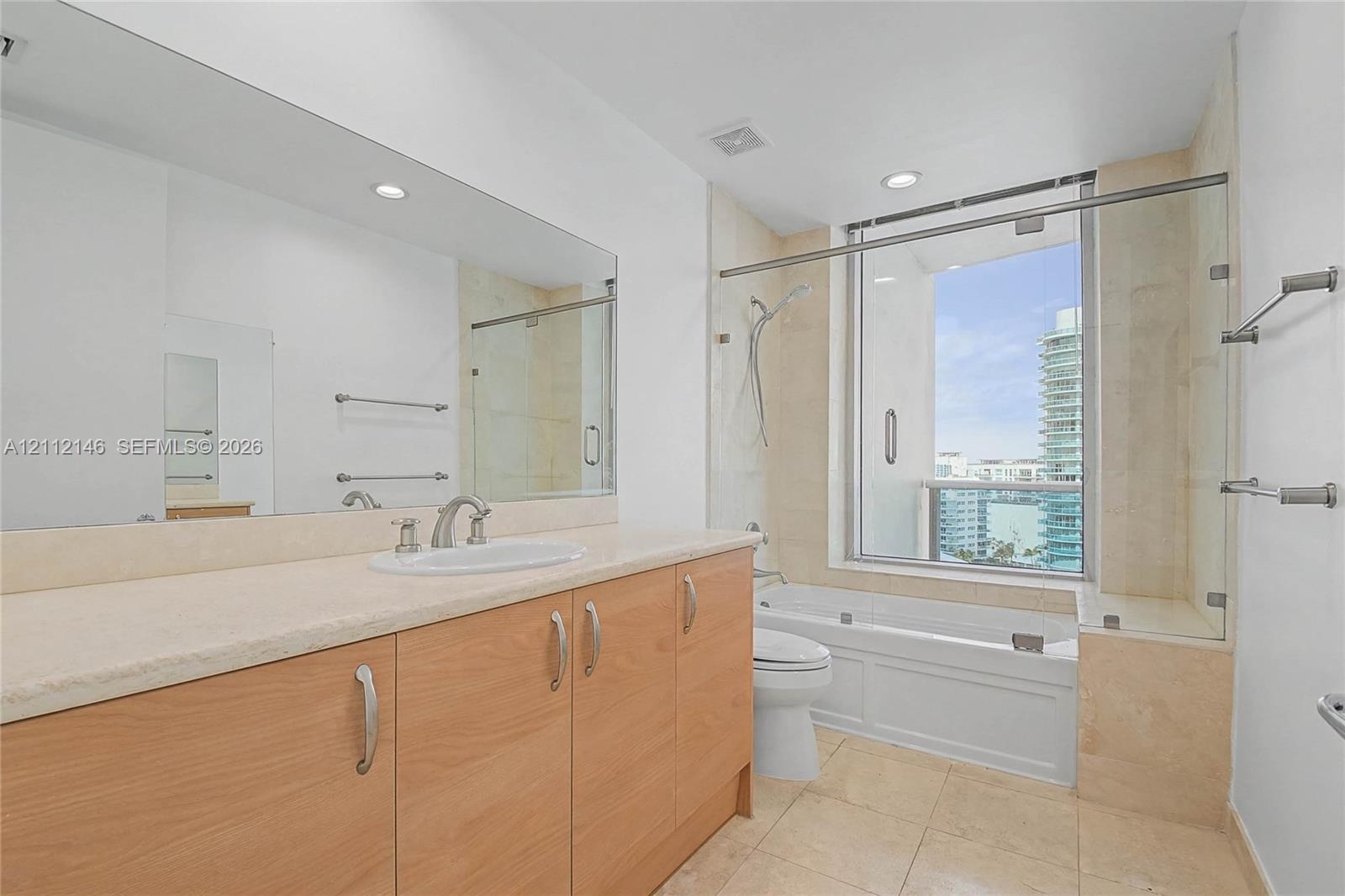Bathroom featuring a light wood-finish vanity, stone-surfaced countertop, oversized wall mirror, tile flooring, and a combined tub and shower enclosur