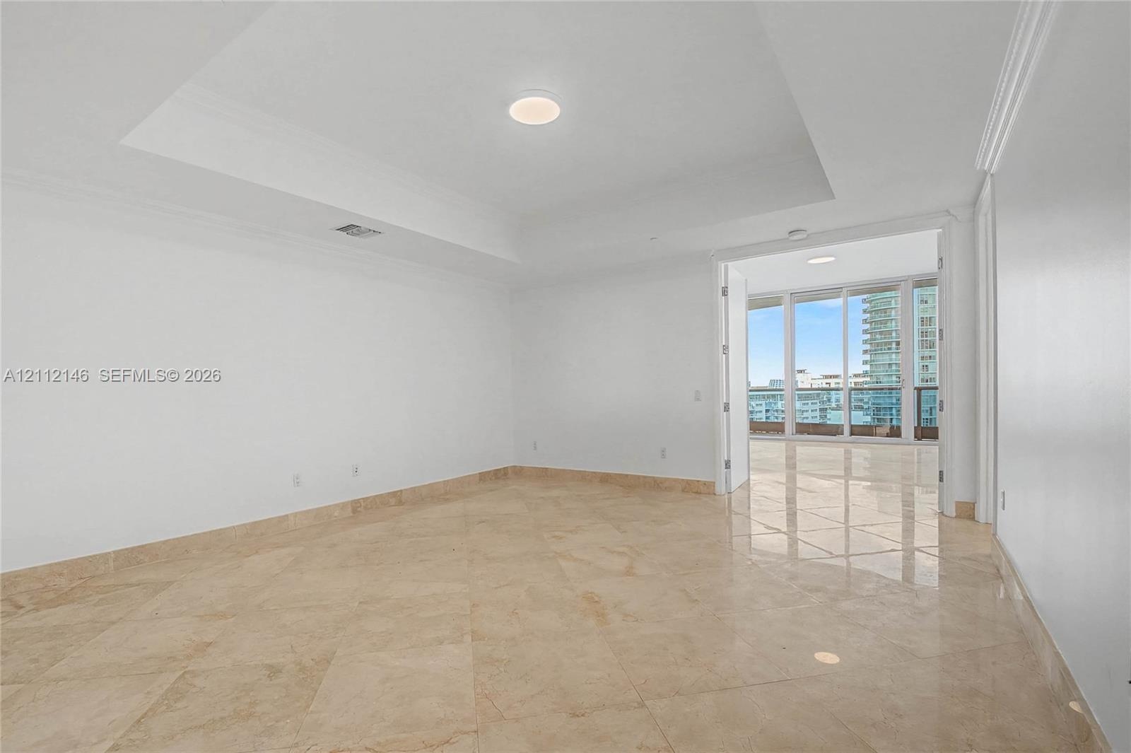 Tray ceiling, neutral stone flooring, and floor-to-ceiling glass doors opening to a terrace