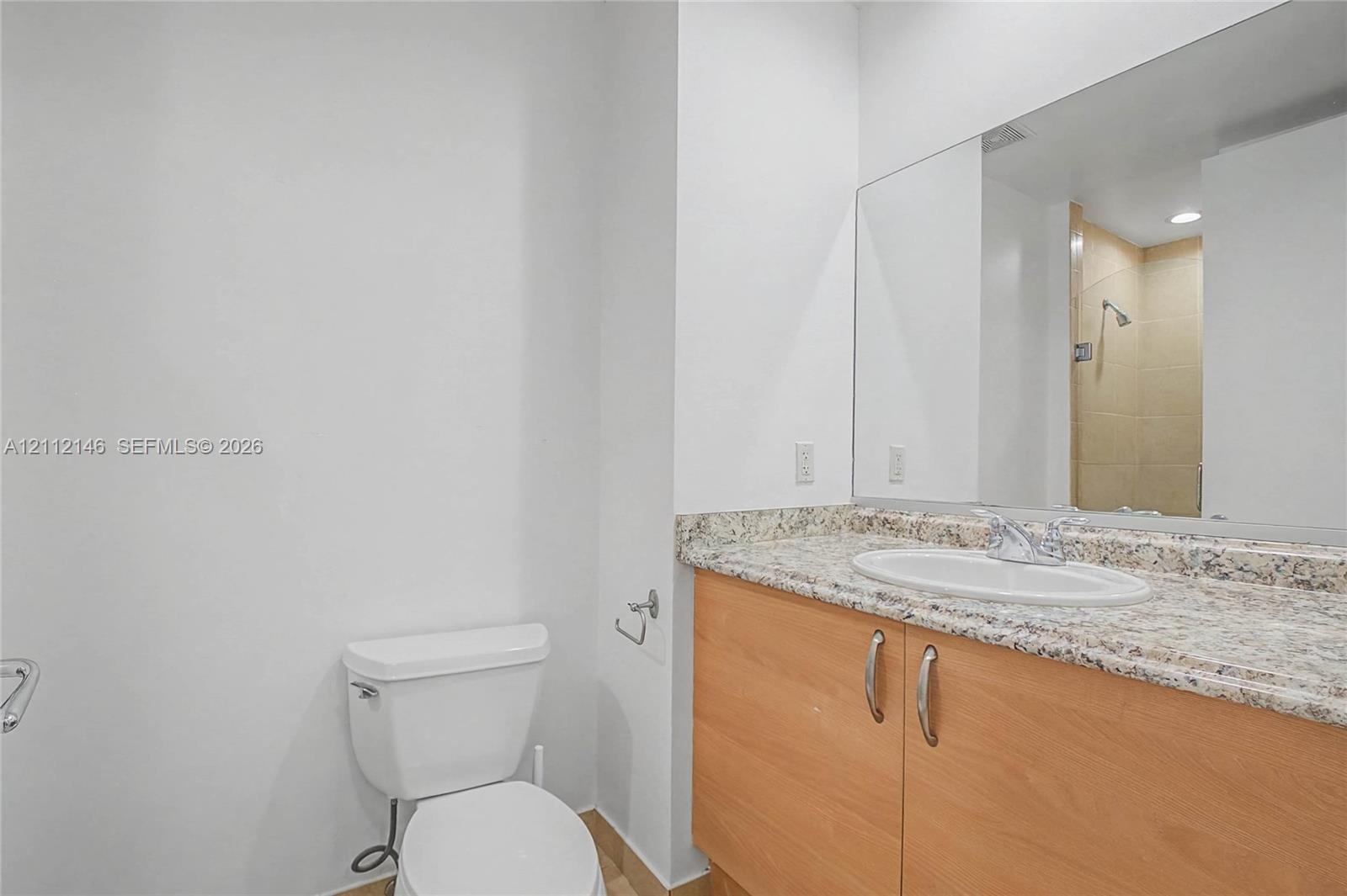 Bathroom featuring a vanity with light-tone wood-finish cabinetry, a neutral-toned stone countertop, an integrated oval sink, and a large-format vanit