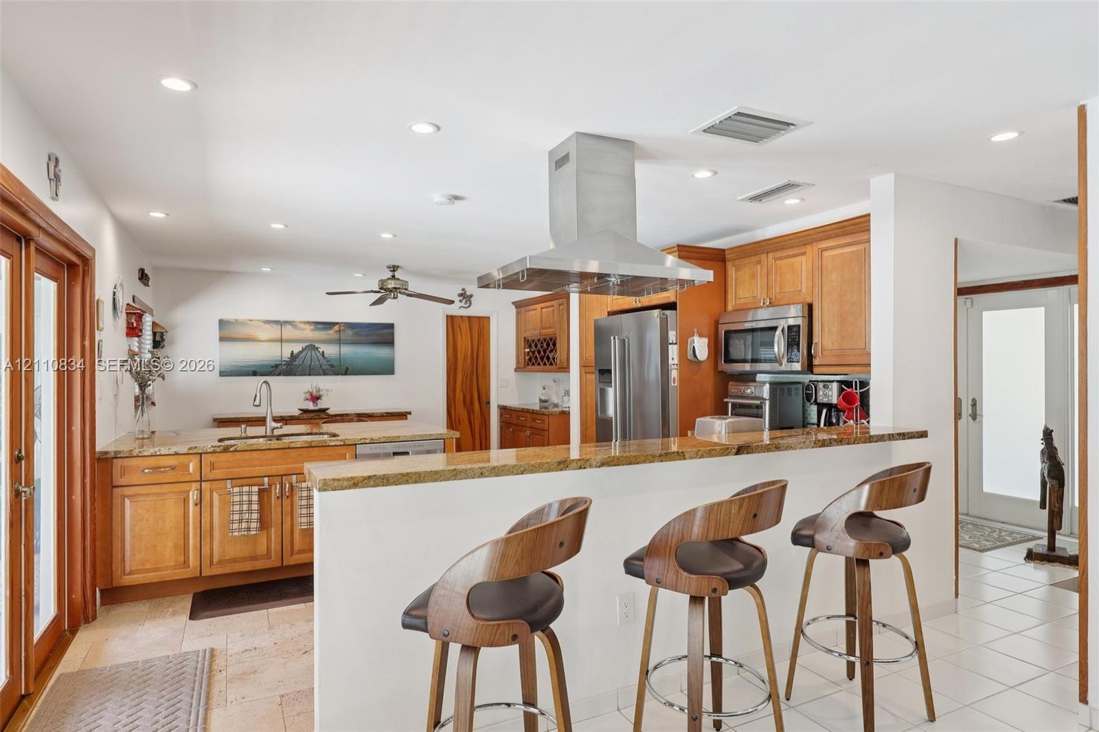 Kitchen featuring wood cabinetry, stone countertops, a raised breakfast bar, a stainless steel chimney-style range hood, and tile flooring