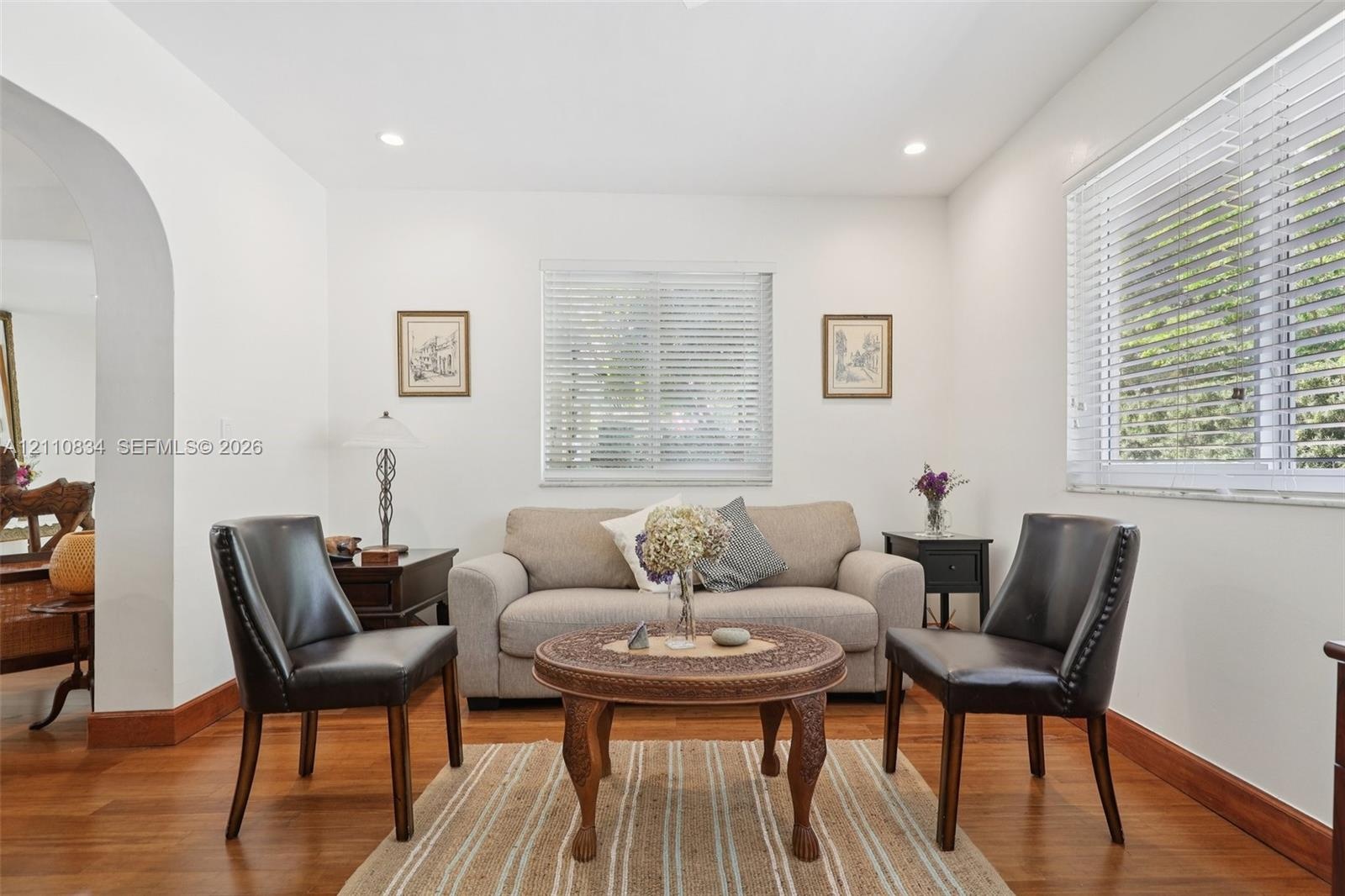Room featuring wood-finish flooring, recessed lighting, white walls, horizontal window blinds, and an arched architectural opening