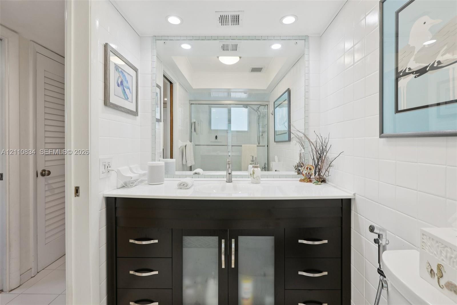 Bathroom featuring a dark wood-finish vanity with an integrated basin, white solid-surface countertop, recessed lighting, and a floor-to-ceiling mirro