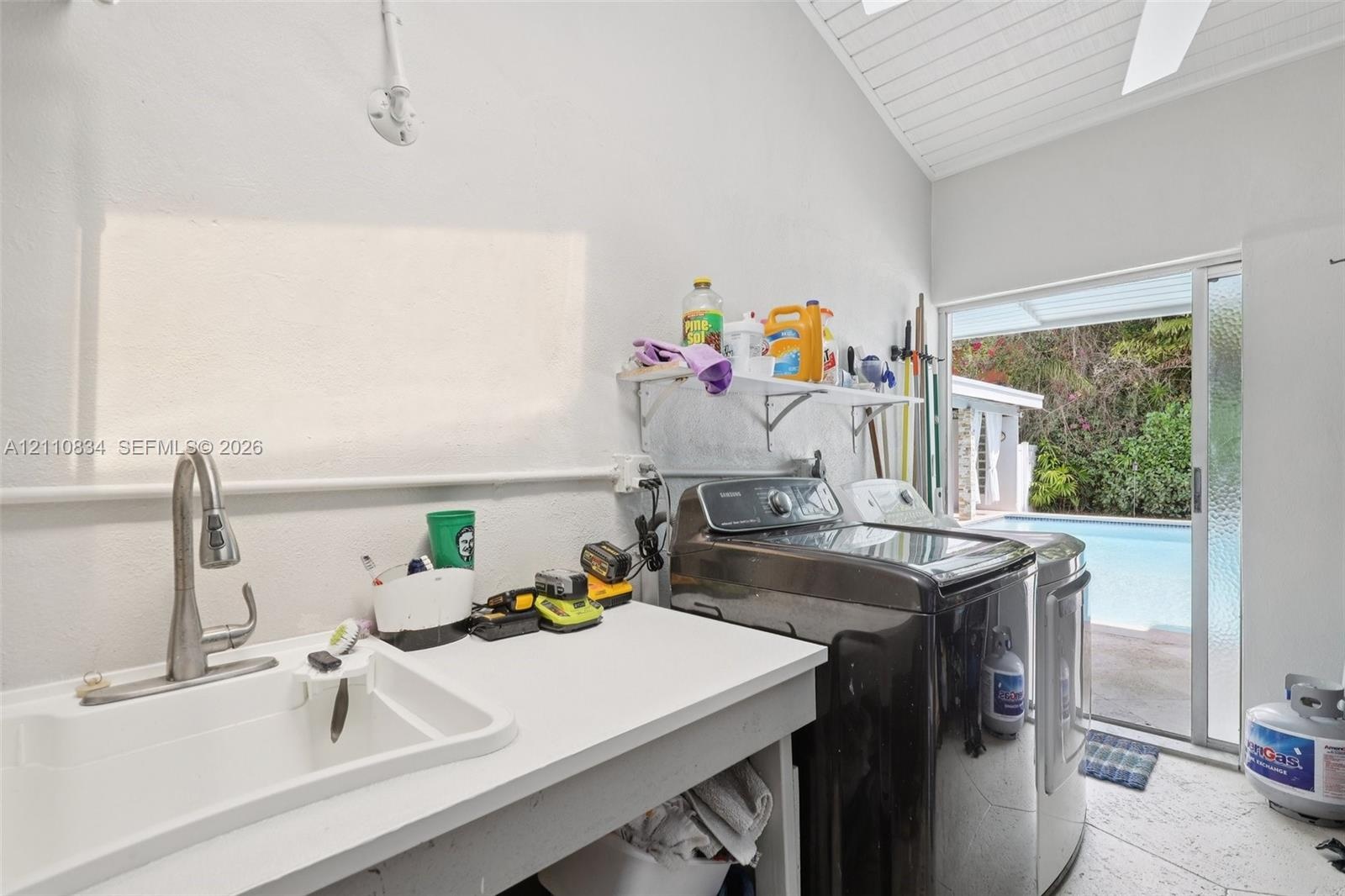 Laundry area featuring a utility sink with a high-arch pull-down faucet, vaulted ceiling with tongue-and-groove finish, tile flooring, and glass slidi