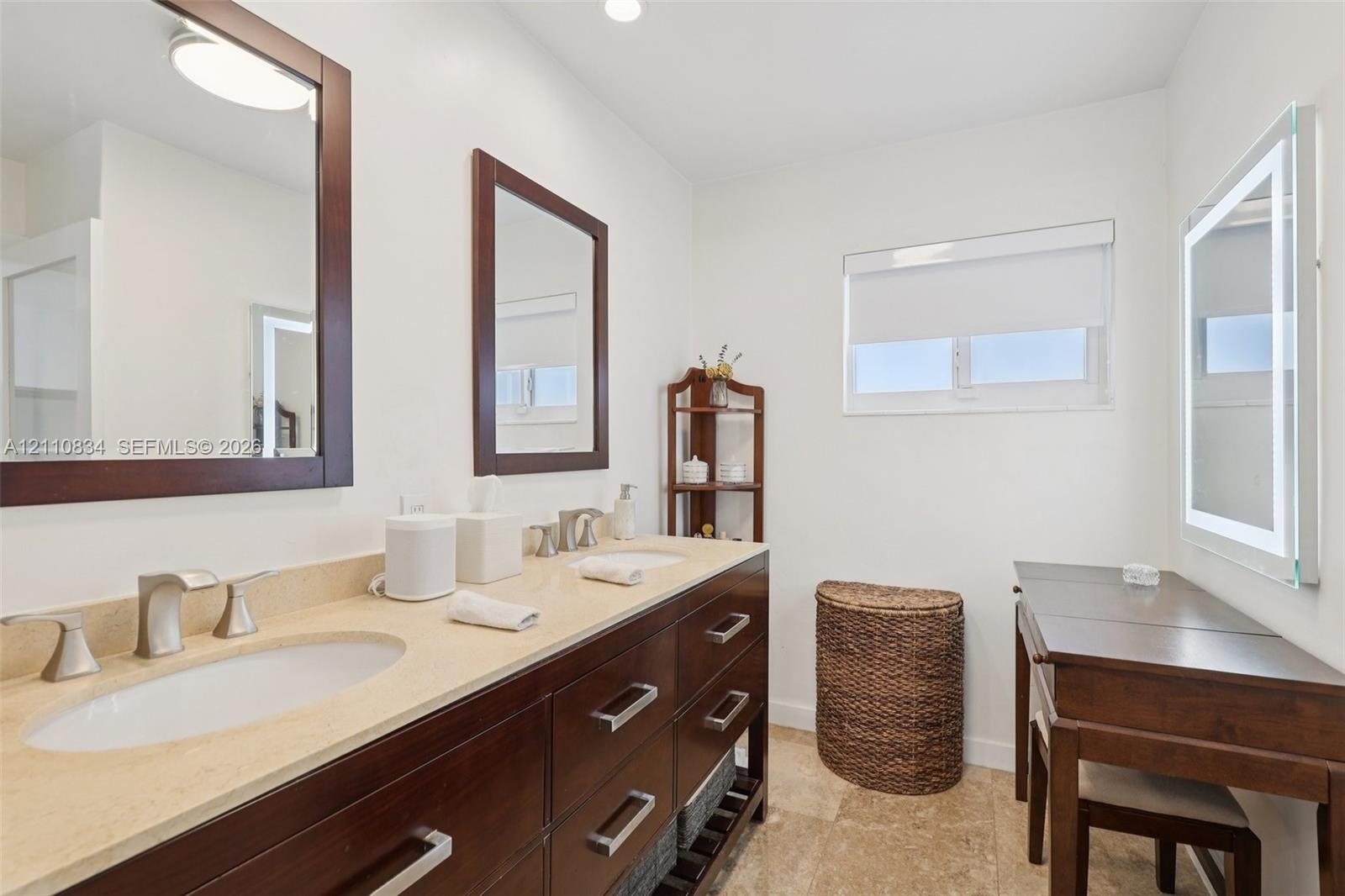 Double vanity with dark wood cabinetry, light-toned stone countertop, dual undermount sinks, and polished chrome fixtures