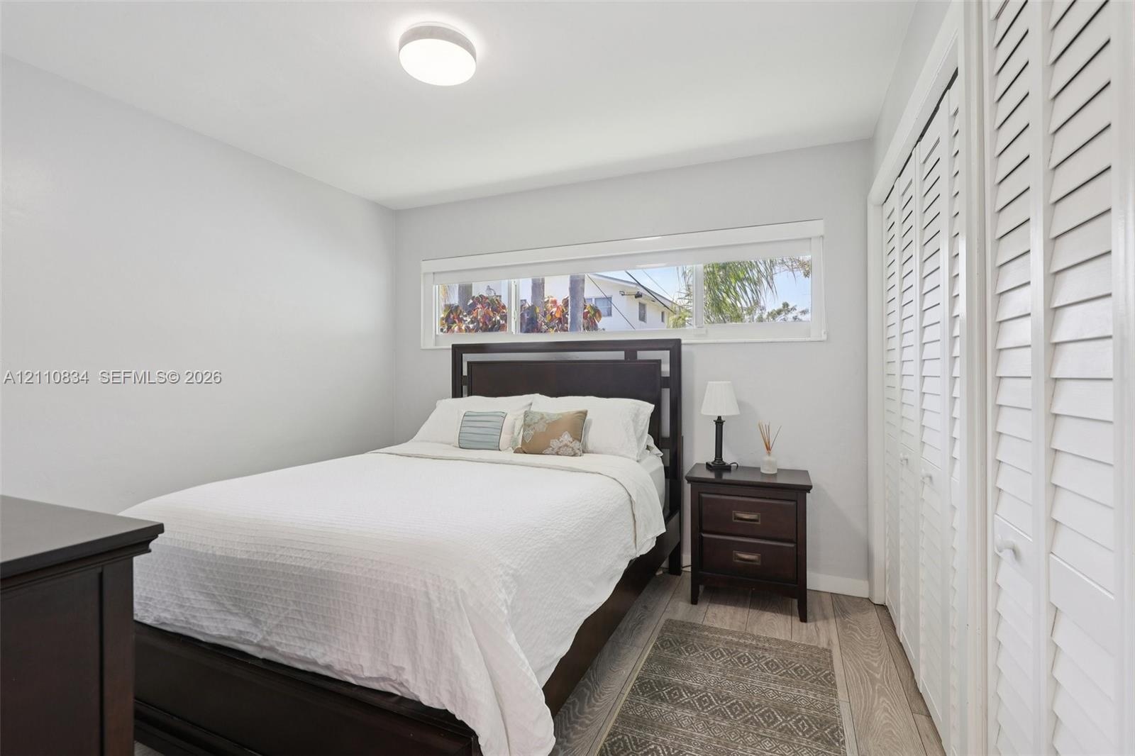 Neutral wall tones, wood-finish flooring, horizontal window, and floor-to-ceiling closet with louvered doors