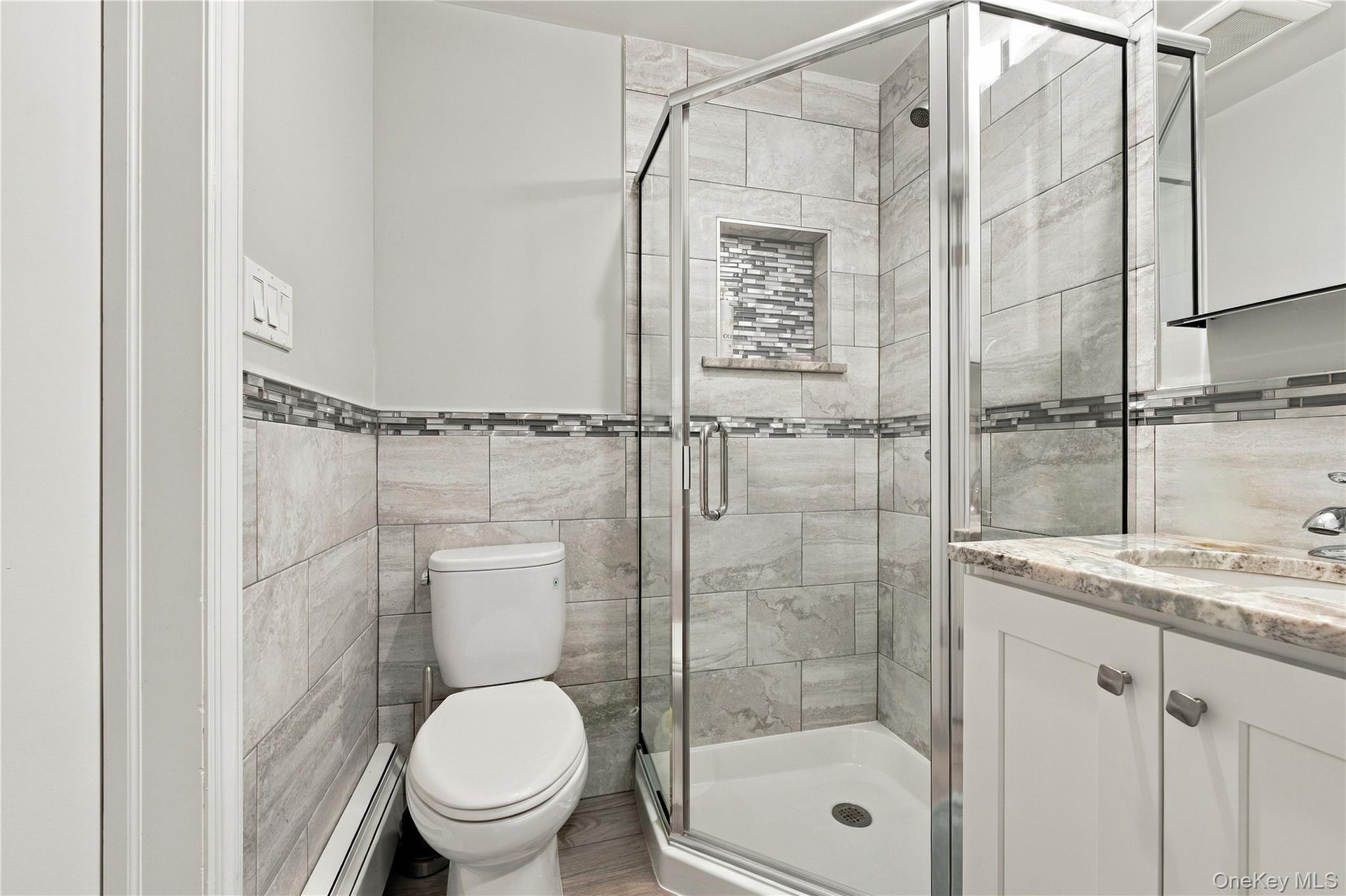 Corner shower featuring a glass enclosure and built-in tiled niche, vanity with stone-finish countertop, and full-height wall tiling with decorative m
