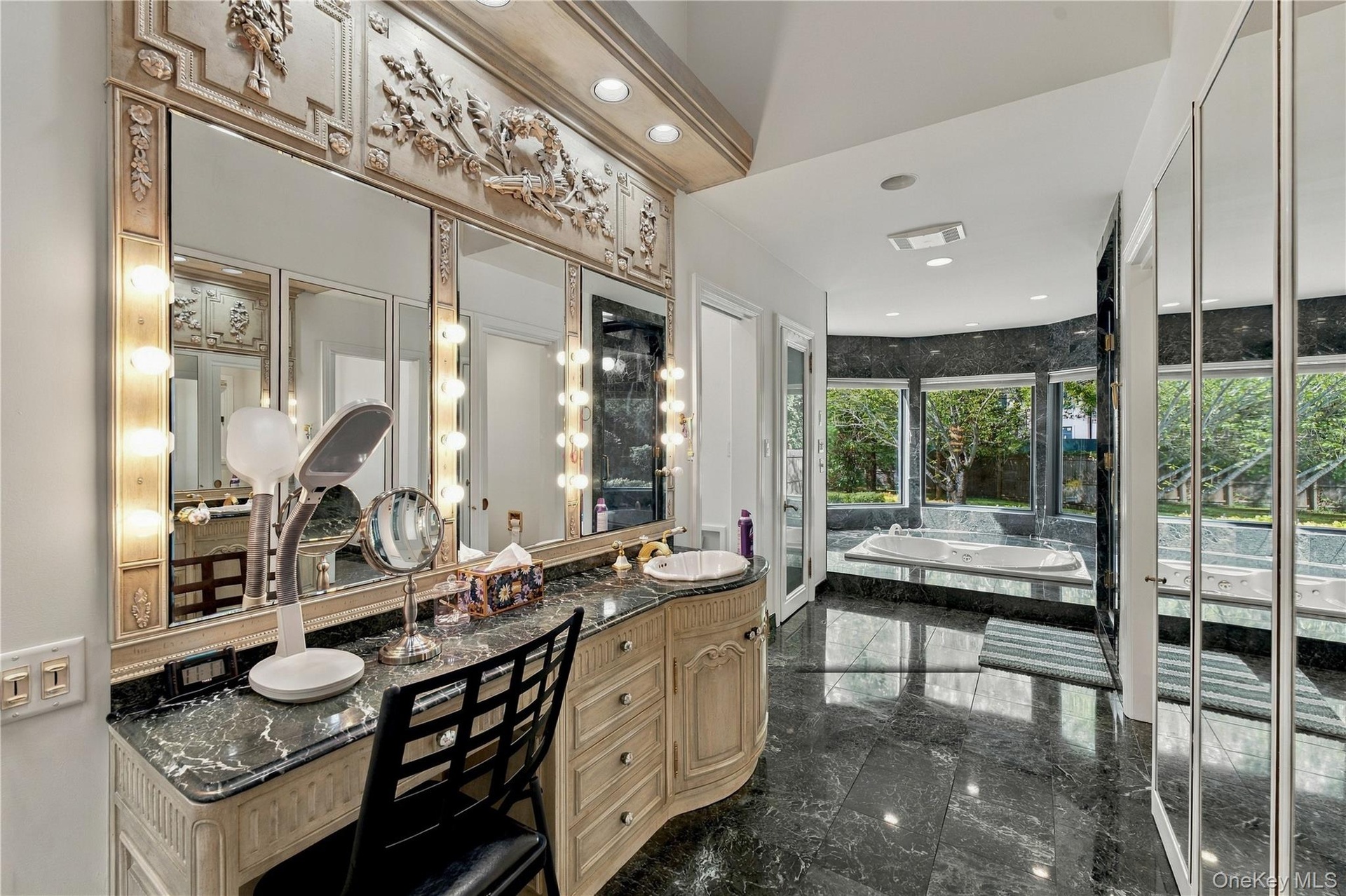 Custom-built vanity with stone countertop and integrated lighting, featuring an ornate architectural mirror frame, polished stone flooring, and a jett