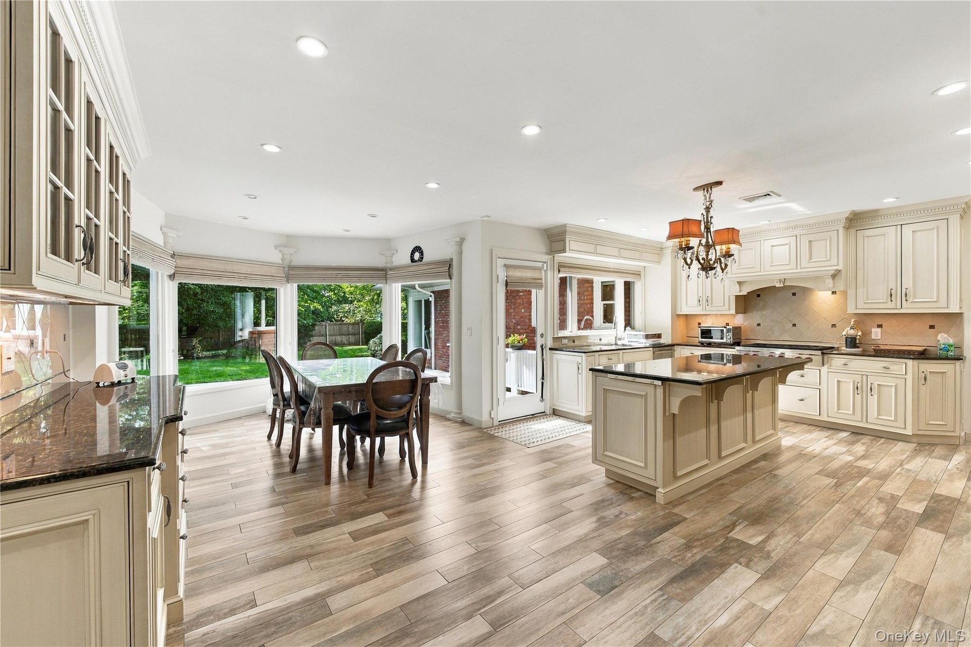 Kitchen featuring wood-finish flooring, custom cabinetry, central island with stone countertop, tile backsplash, and bay windows