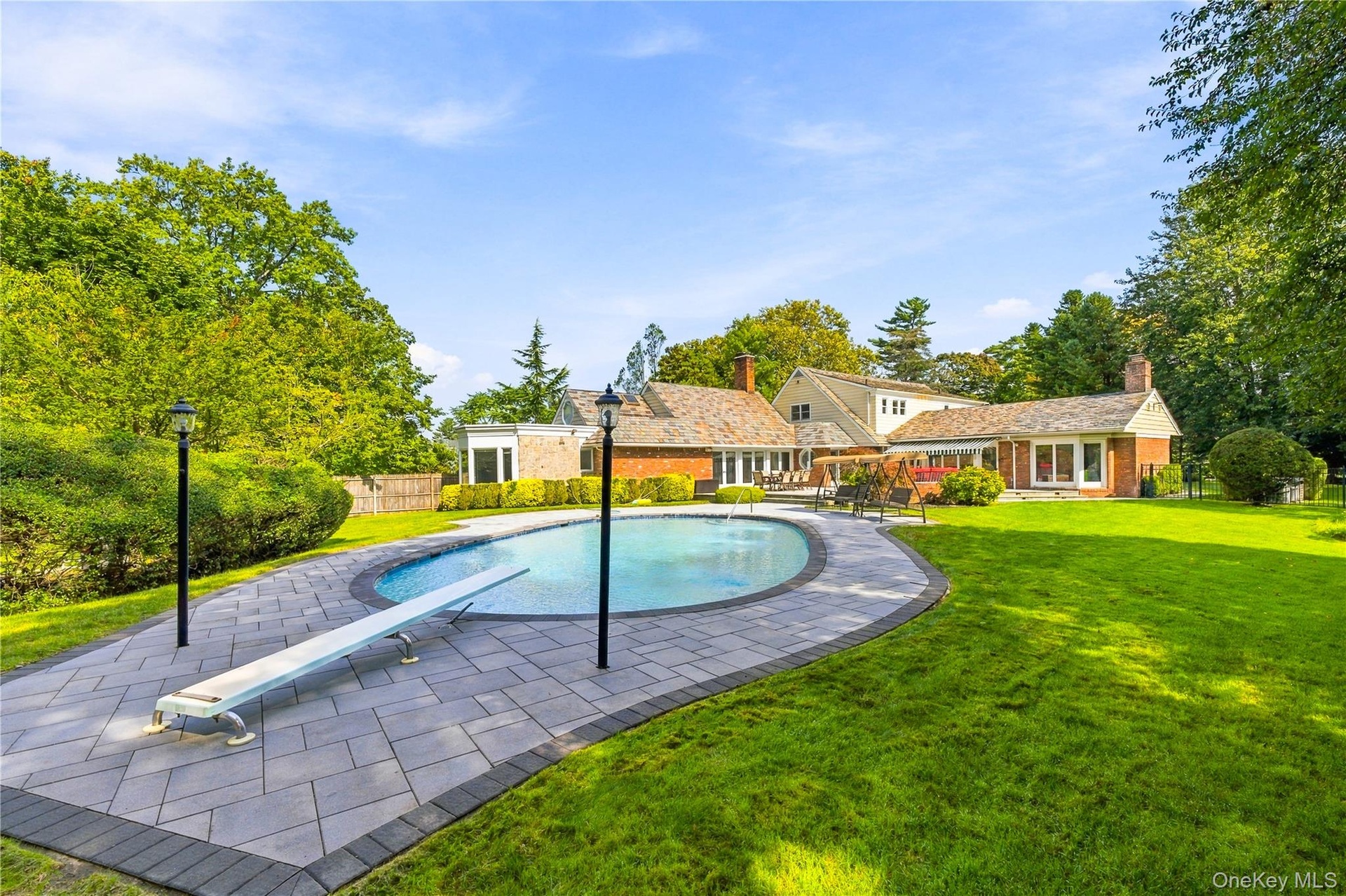 Backyard grounds featuring an inground swimming pool with a diving board, surrounding paver patio, and expansive lawn area