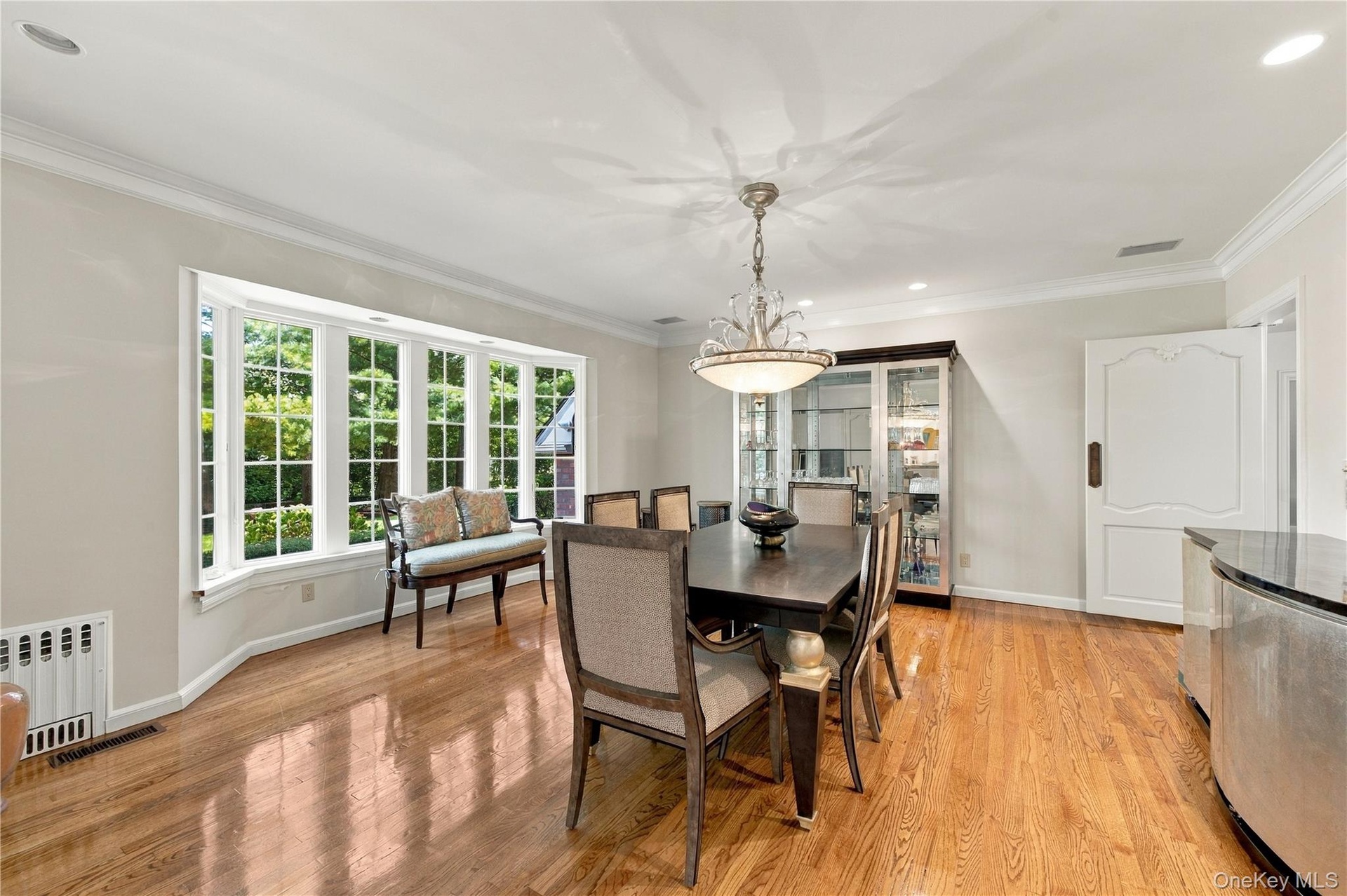 Dining area featuring wood-finish flooring, a multi-pane bay window, crown molding, and an overhead chandelier with crystal accents