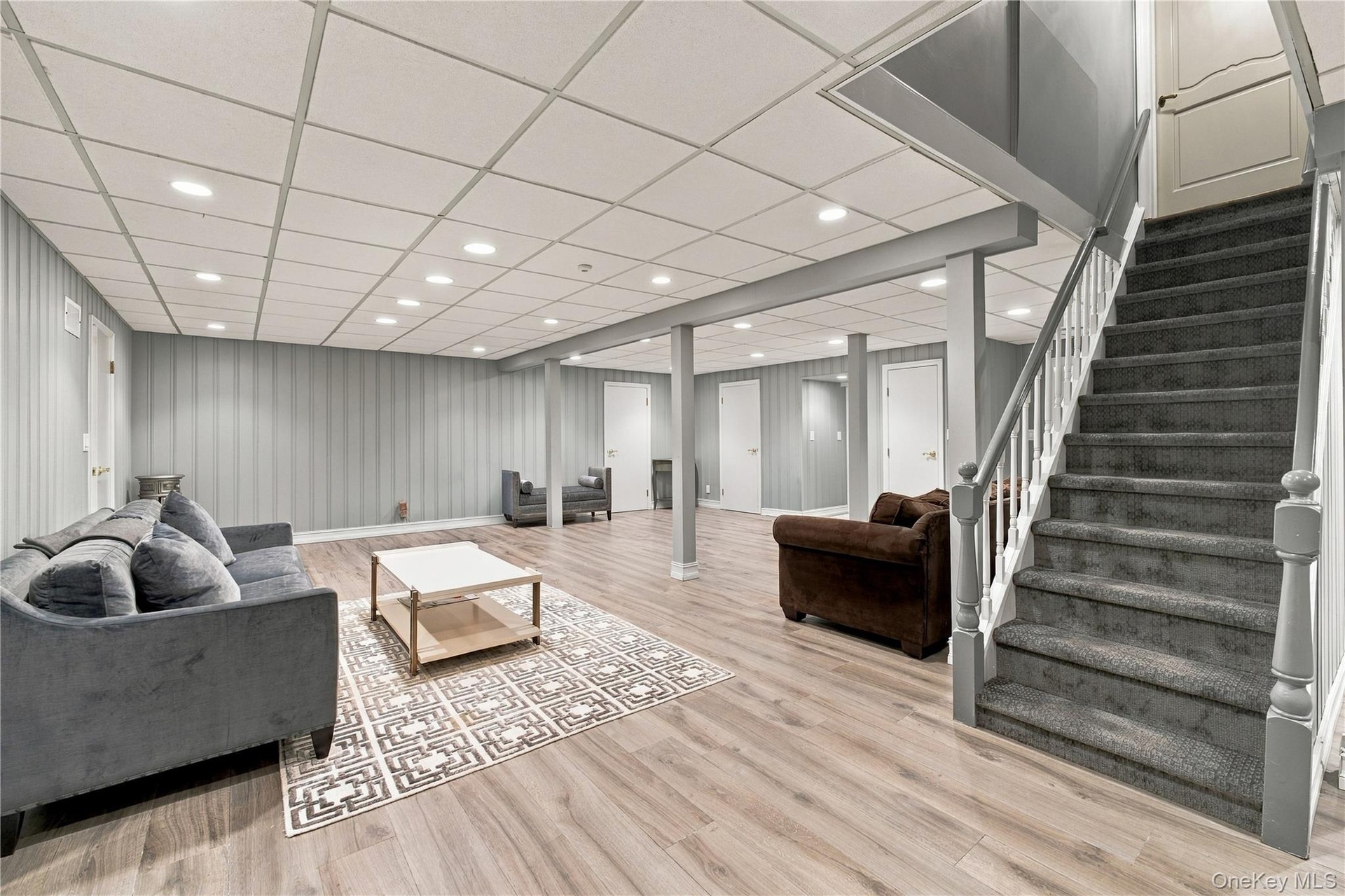 Finished space featuring wood-finish flooring, a drop ceiling with recessed lighting, vertical paneled wall treatments, and a carpeted staircase with 
