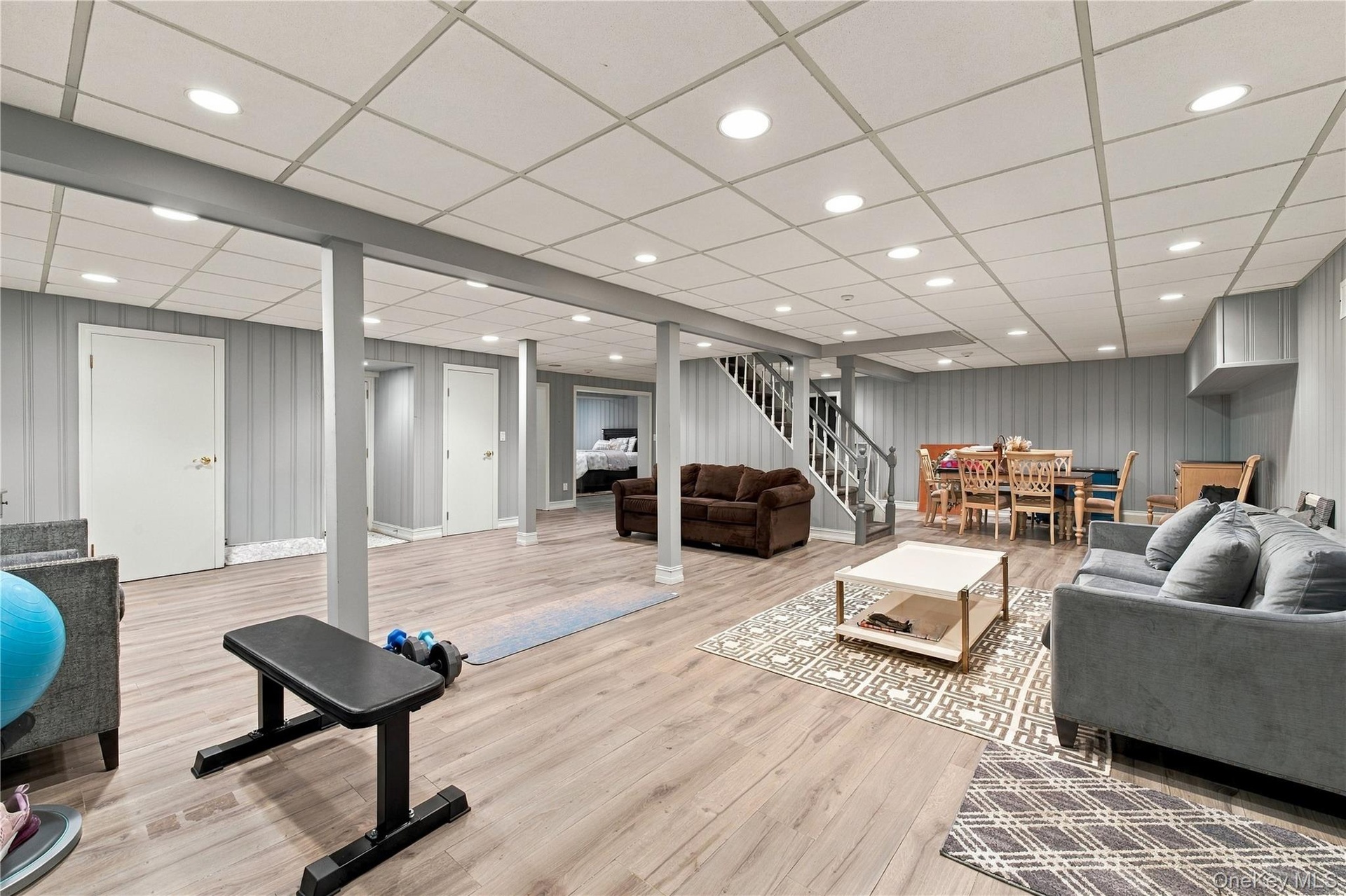 Finished lower level with wood-finish flooring, recessed lighting, vertical paneling, and a staircase featuring wood railings