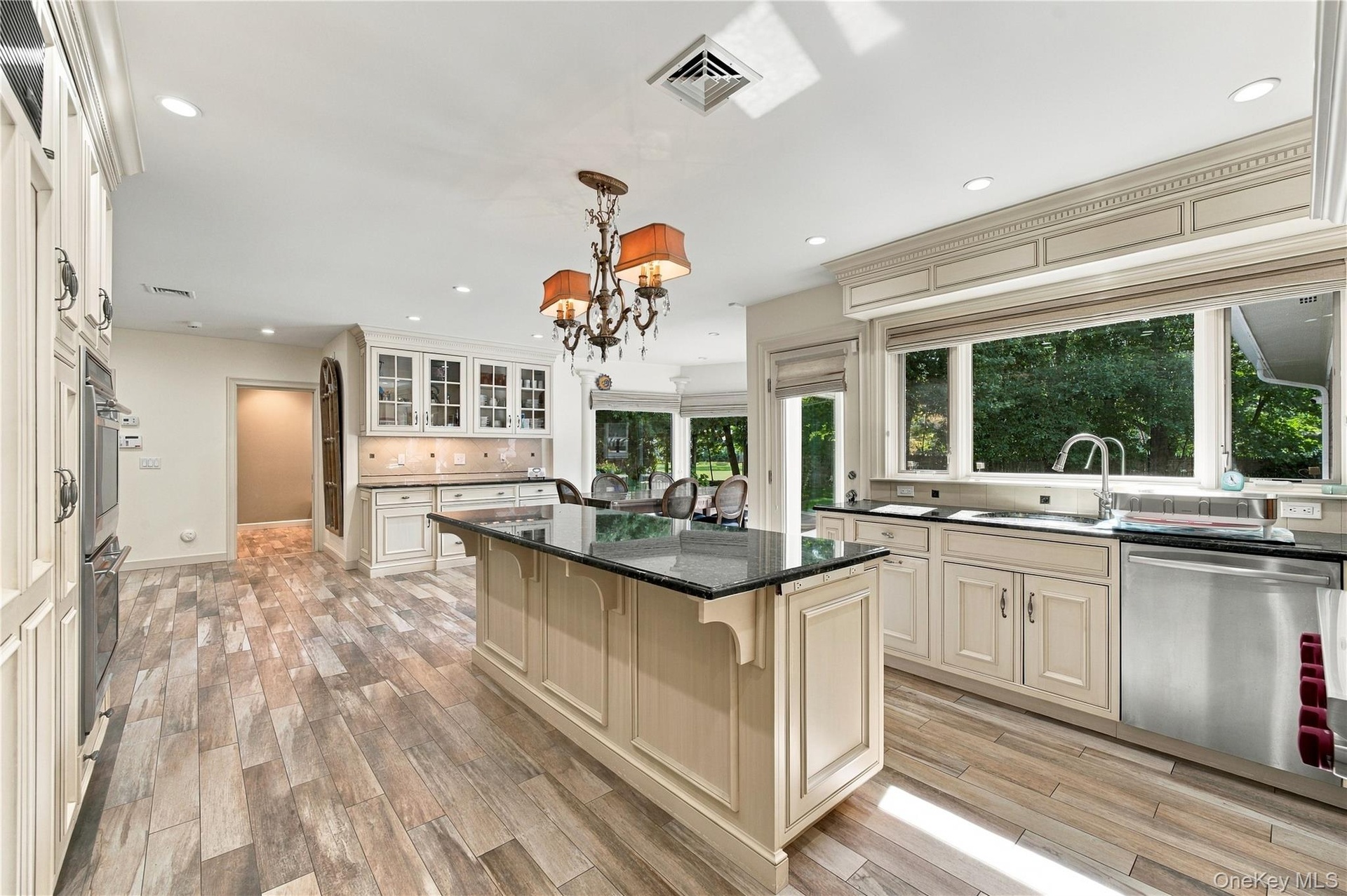 Kitchen featuring custom cabinetry with crown molding, a center island with a dark stone countertop, stainless steel appliances, wood-finish flooring,