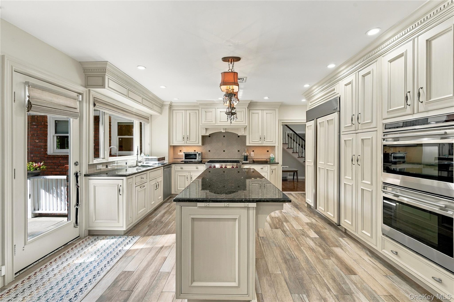 Kitchen featuring light-toned recessed-panel cabinetry, a central island with stone-finish countertops, stainless steel double wall ovens, wood-finish