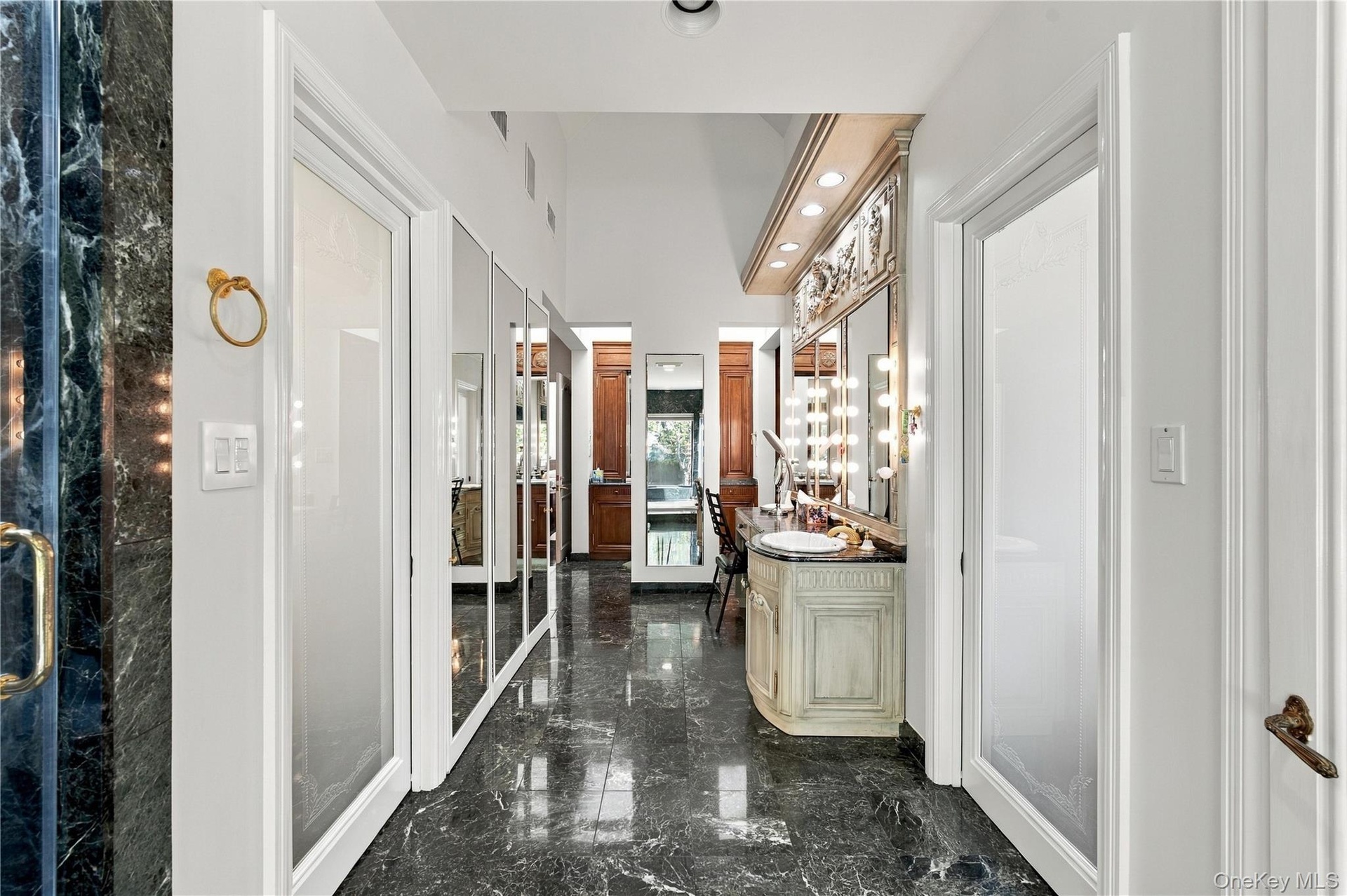 Polished stone flooring, built-in vanity with integrated lighting, full-length mirrored panels, and custom millwork featuring crown molding
