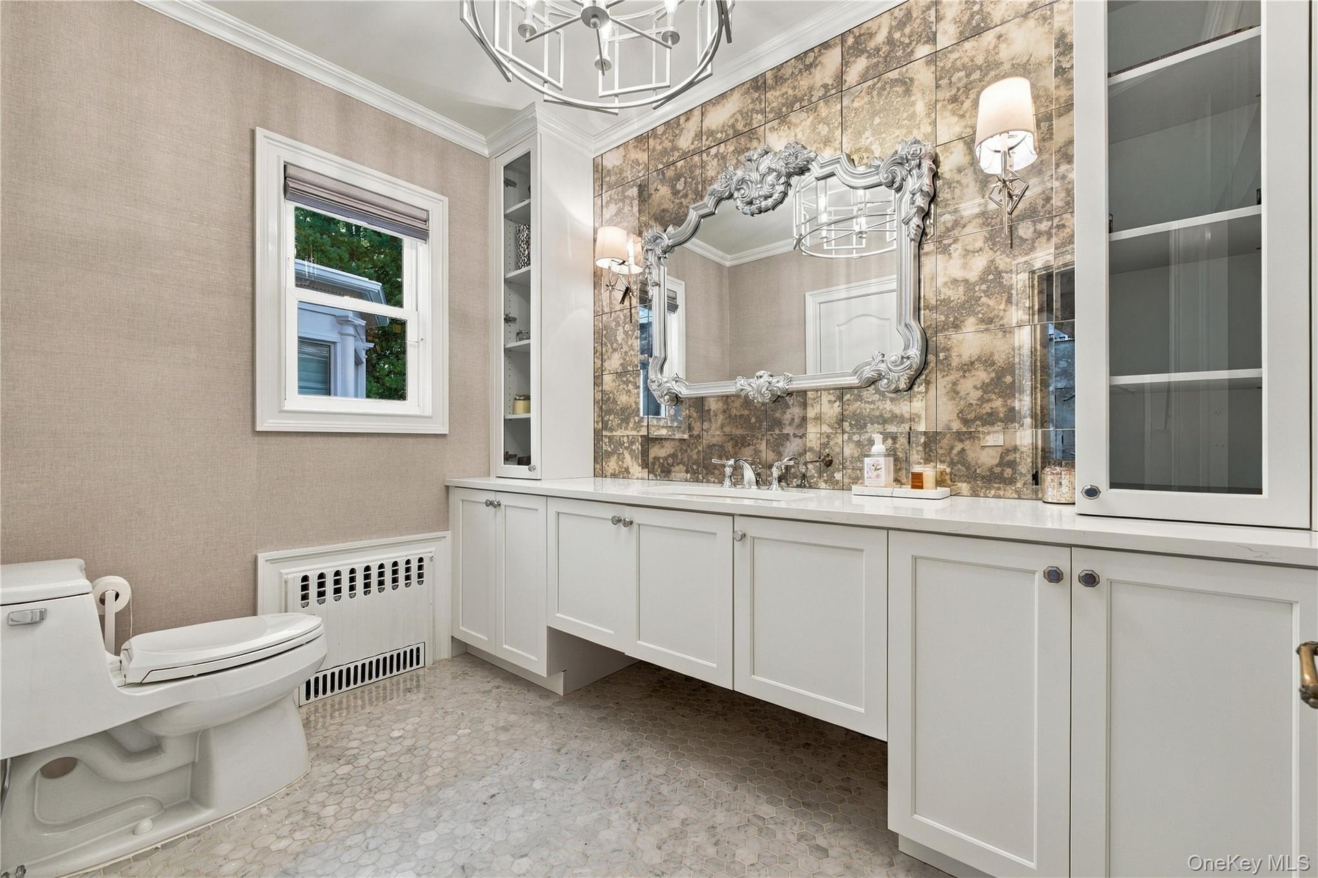 Custom white cabinetry with integrated storage, antique-style mirrored backsplash, metallic light fixtures, and stone-tiled flooring