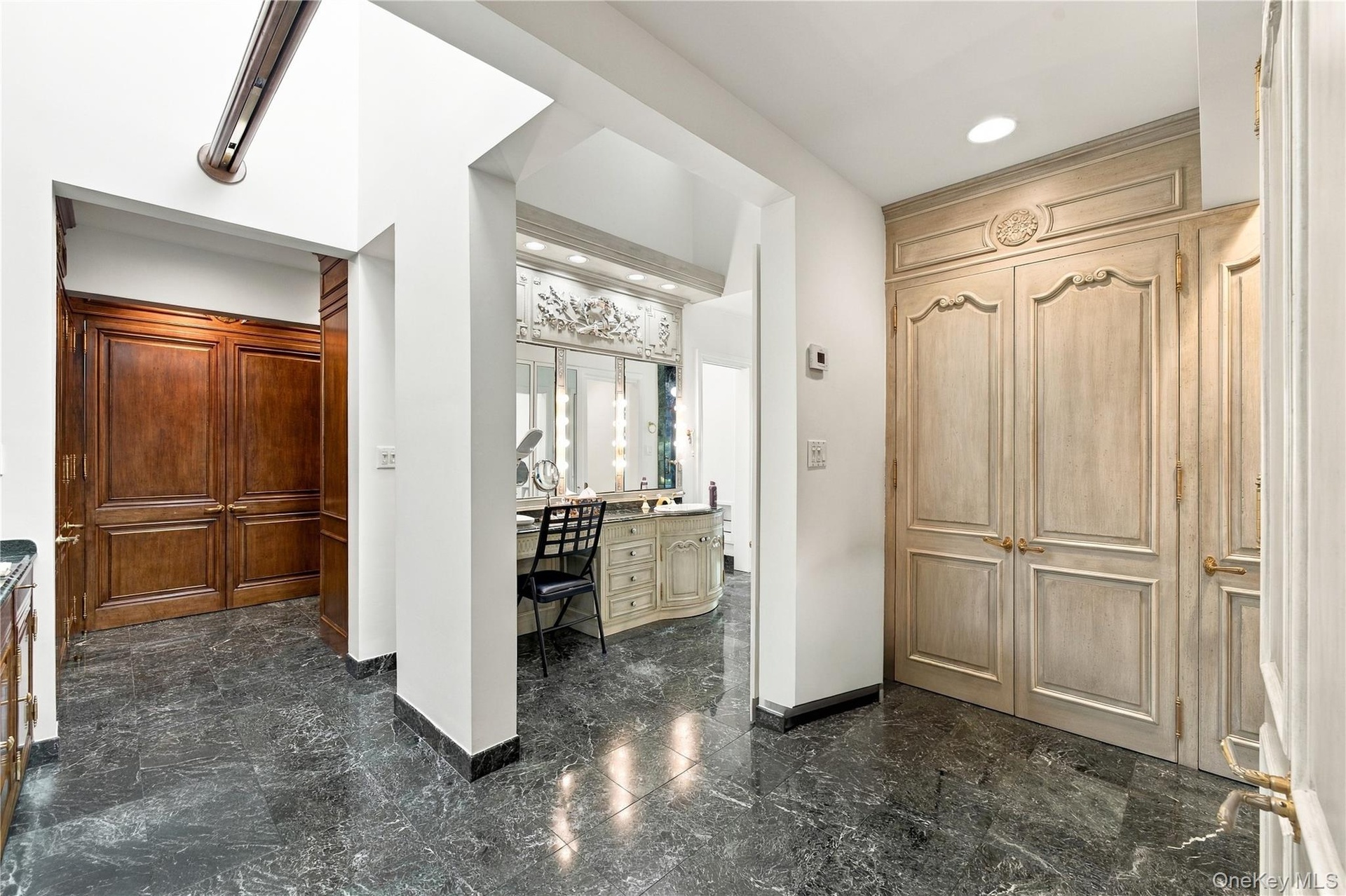 Polished stone flooring, custom floor-to-ceiling cabinetry with ornate detailing, built-in vanity with integrated lighting, and stained wood double do