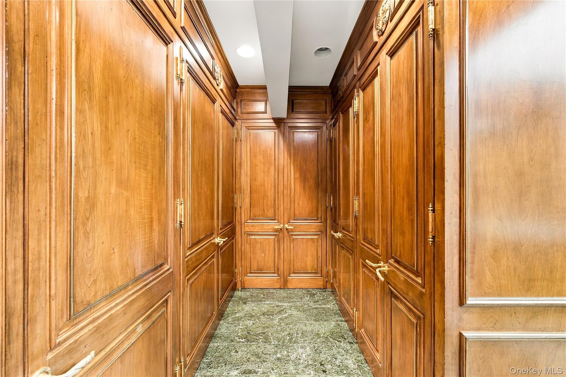 Floor-to-ceiling wood paneling featuring intricate raised-panel detailing, solid wood double doors, decorative brass hardware, and polished stone floo
