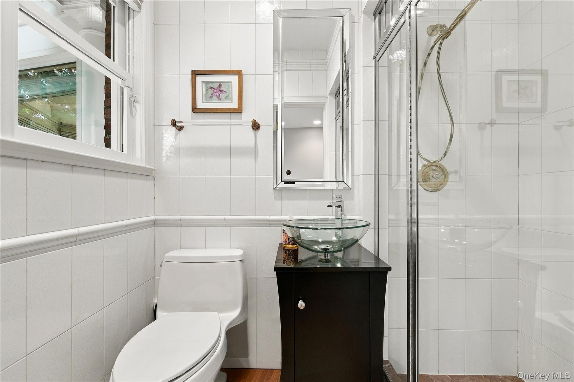 Bathroom featuring white wall tiling with chair rail molding, a dark wood-finish vanity with a glass vessel sink, a chrome faucet, and a glass-enclose