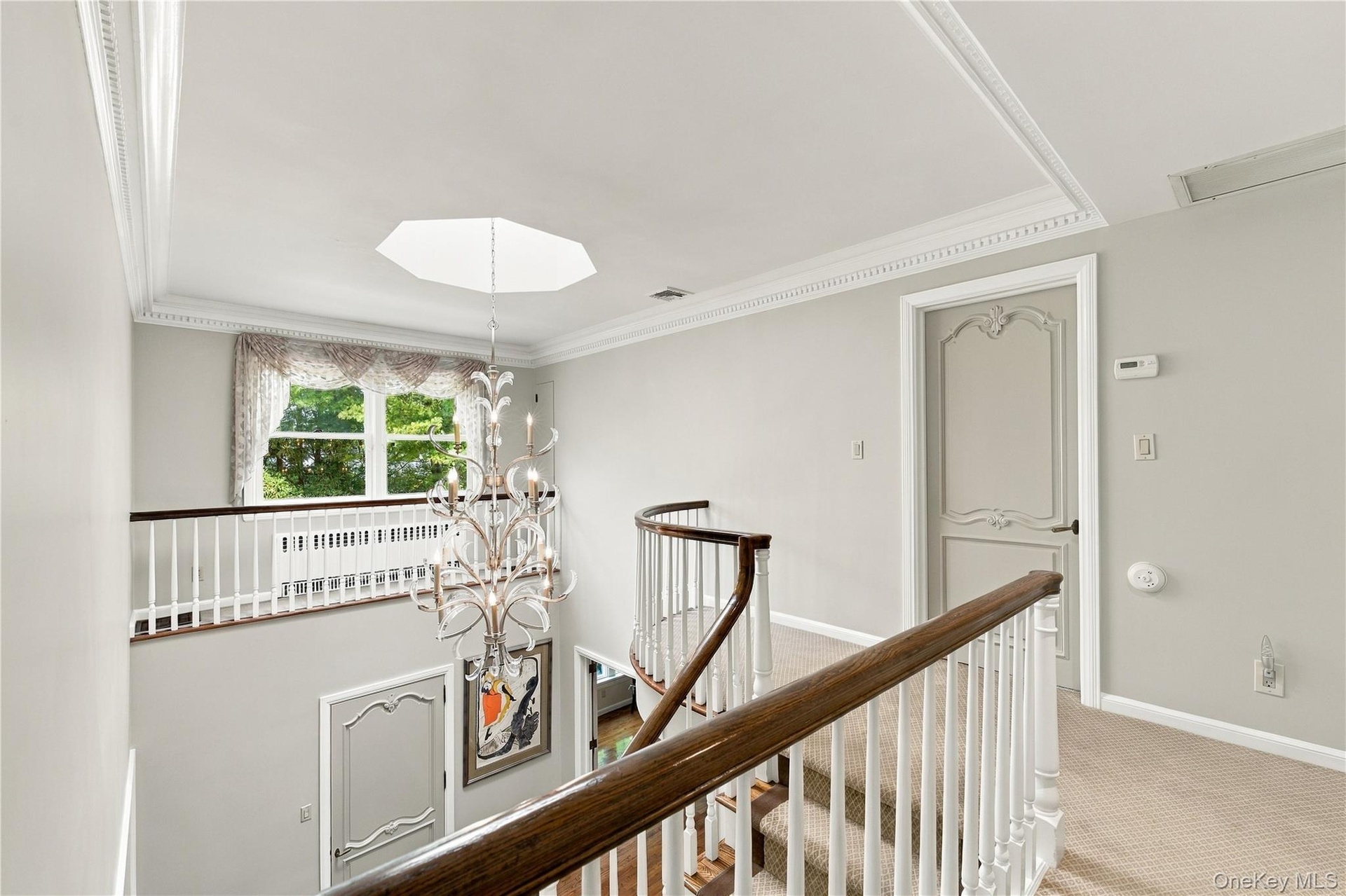 Open landing featuring tiered crown molding, a decorative metal chandelier, arched-panel interior doors, and a curved staircase with a wood handrail