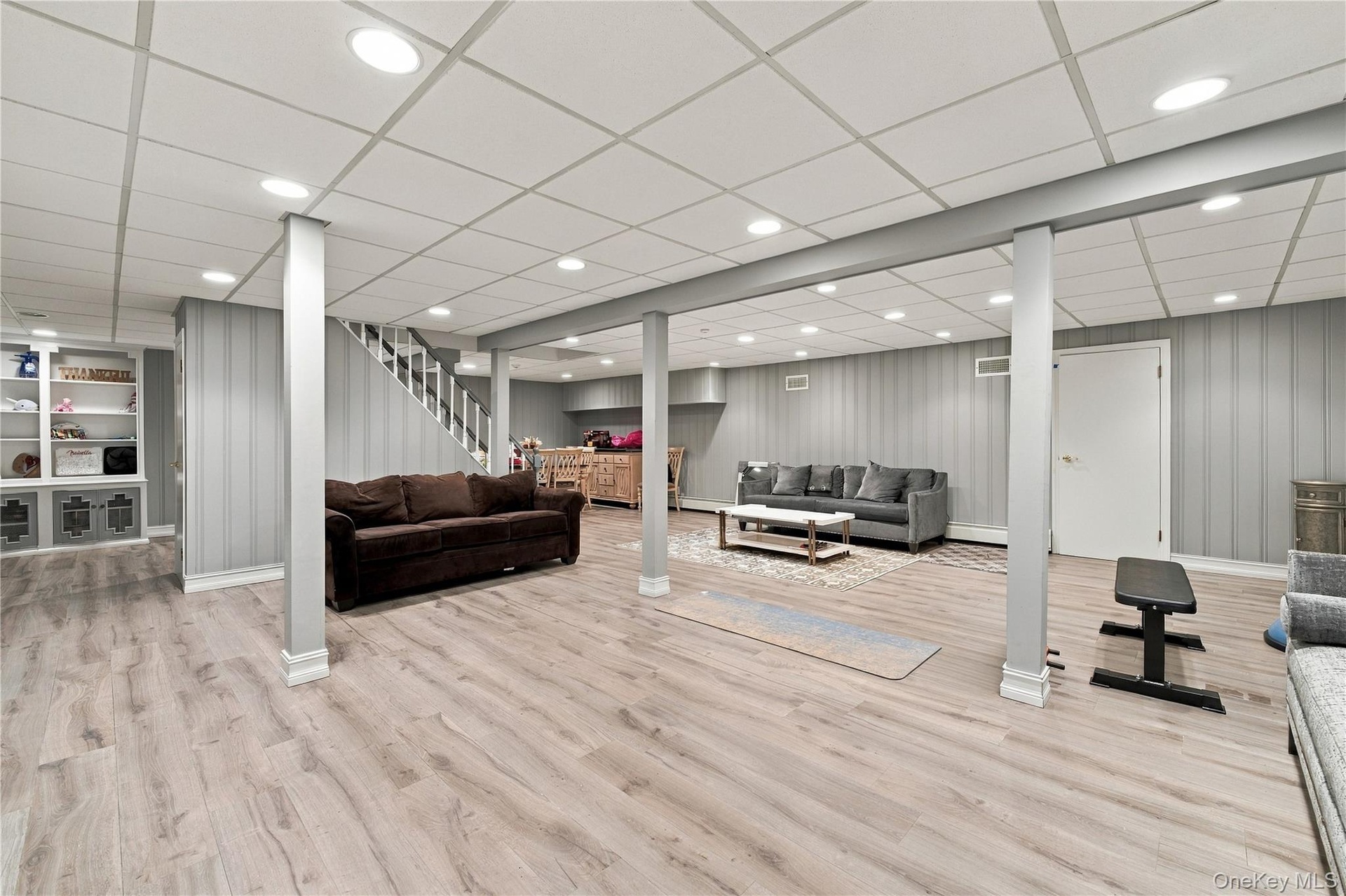 Finished lower level featuring wood-finish flooring, recessed lighting, drop ceiling, vertical paneling, and built-in shelving