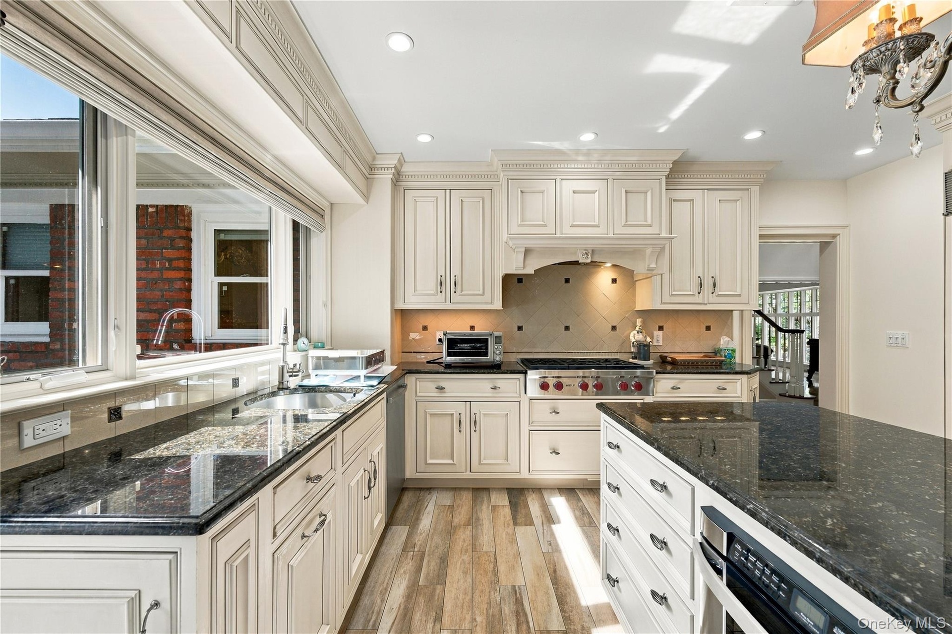Kitchen featuring cream-toned cabinetry with crown molding, dark stone countertops, wood-finish flooring, a stainless steel range with a custom hood e
