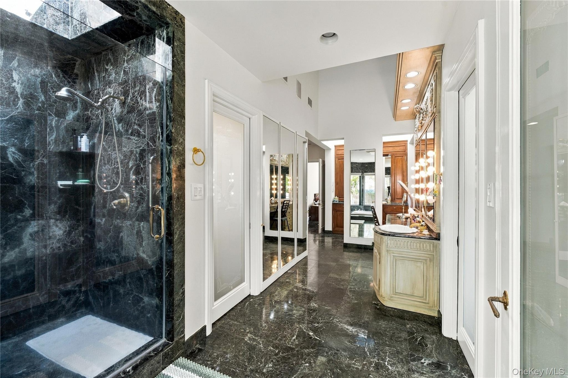 Enclosed shower featuring dark stone tile surround, stone flooring, built-in vanity with integrated lighting, recessed ceiling lighting, and floor-to-