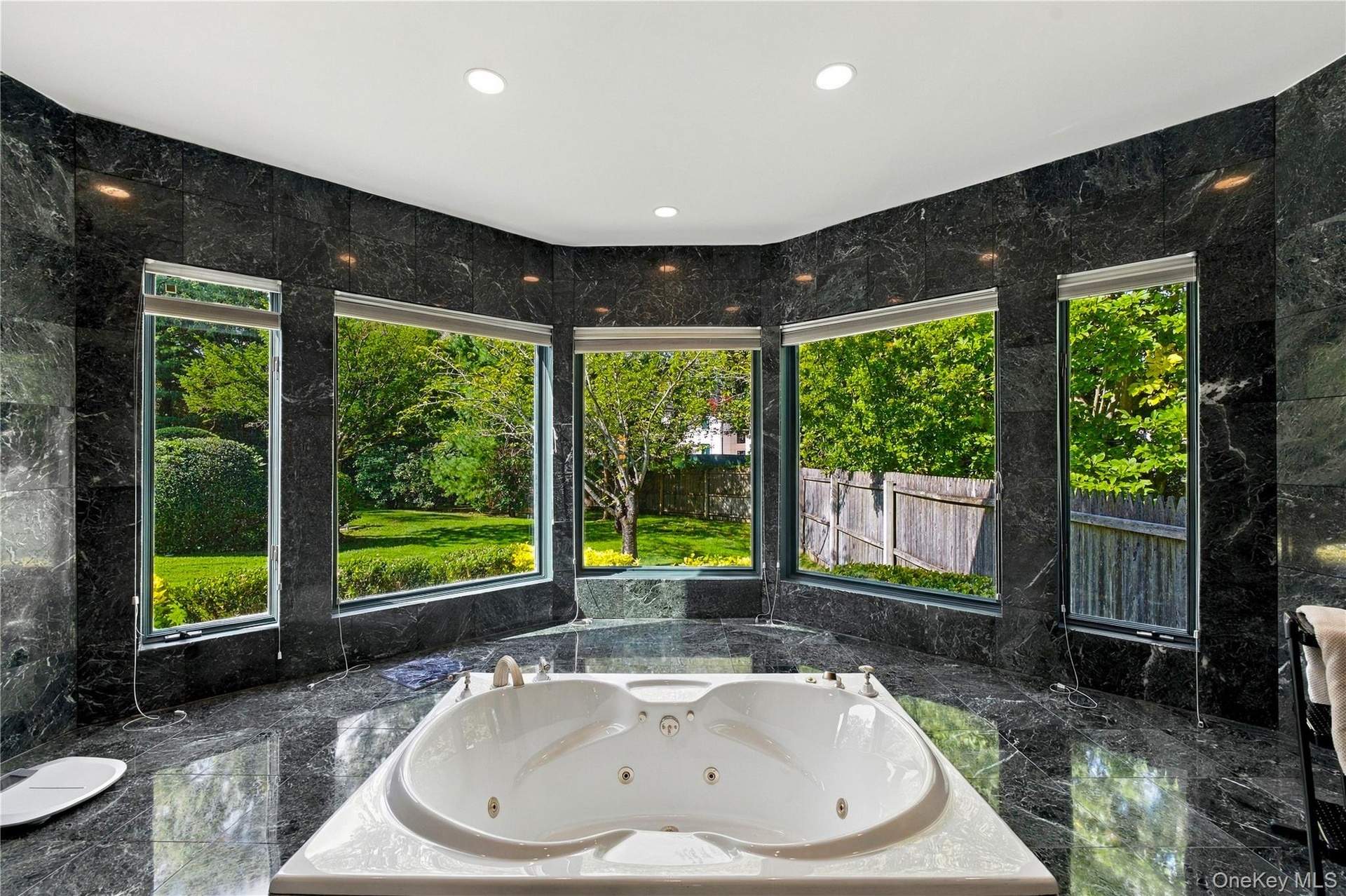 Polished stone wall and floor tiling, expansive multi-panel window configuration, and recessed soaking tub with integrated fixtures