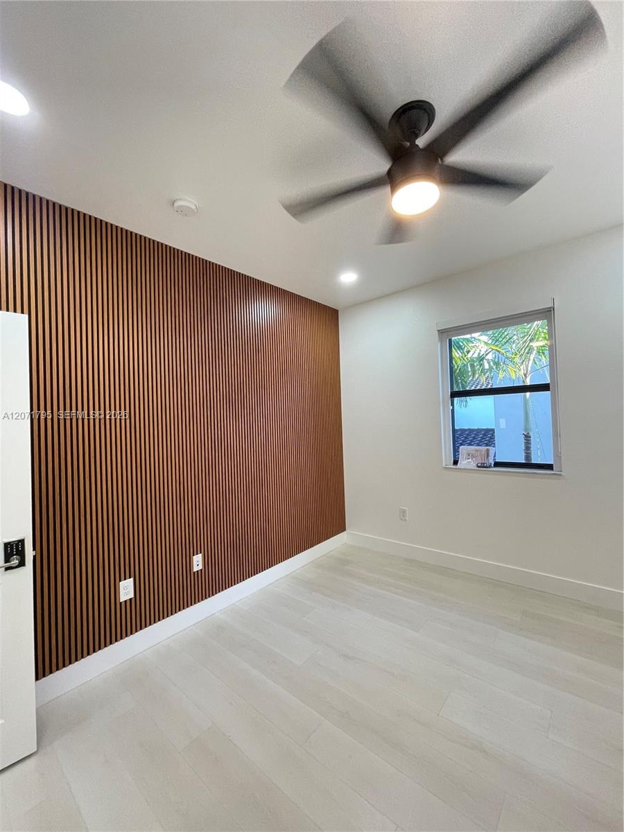 Vertical wood-slat accent wall, light-toned wood-finish flooring, matte black ceiling fan with integrated lighting, and recessed overhead lighting